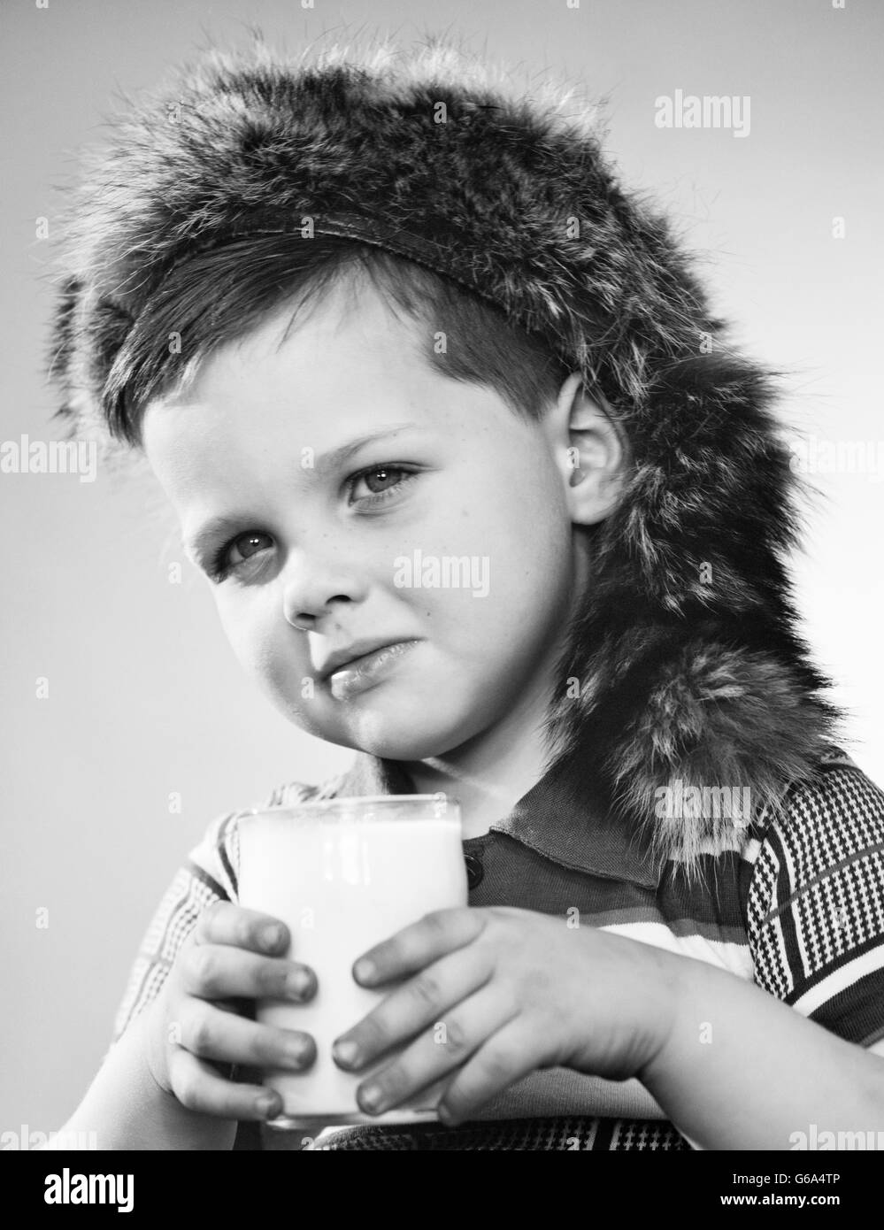 Anni Cinquanta ritratto ragazzo indossa Davy Crockett COONSKIN CAP HOLDING bicchiere di latte guardando la fotocamera Foto Stock