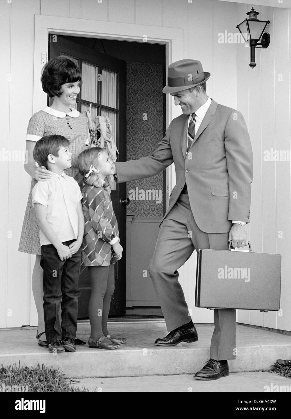 Negli anni sessanta la famiglia permanente sulla parte anteriore passi padre valigetta porta dicendo addio andando al lavoro Foto Stock