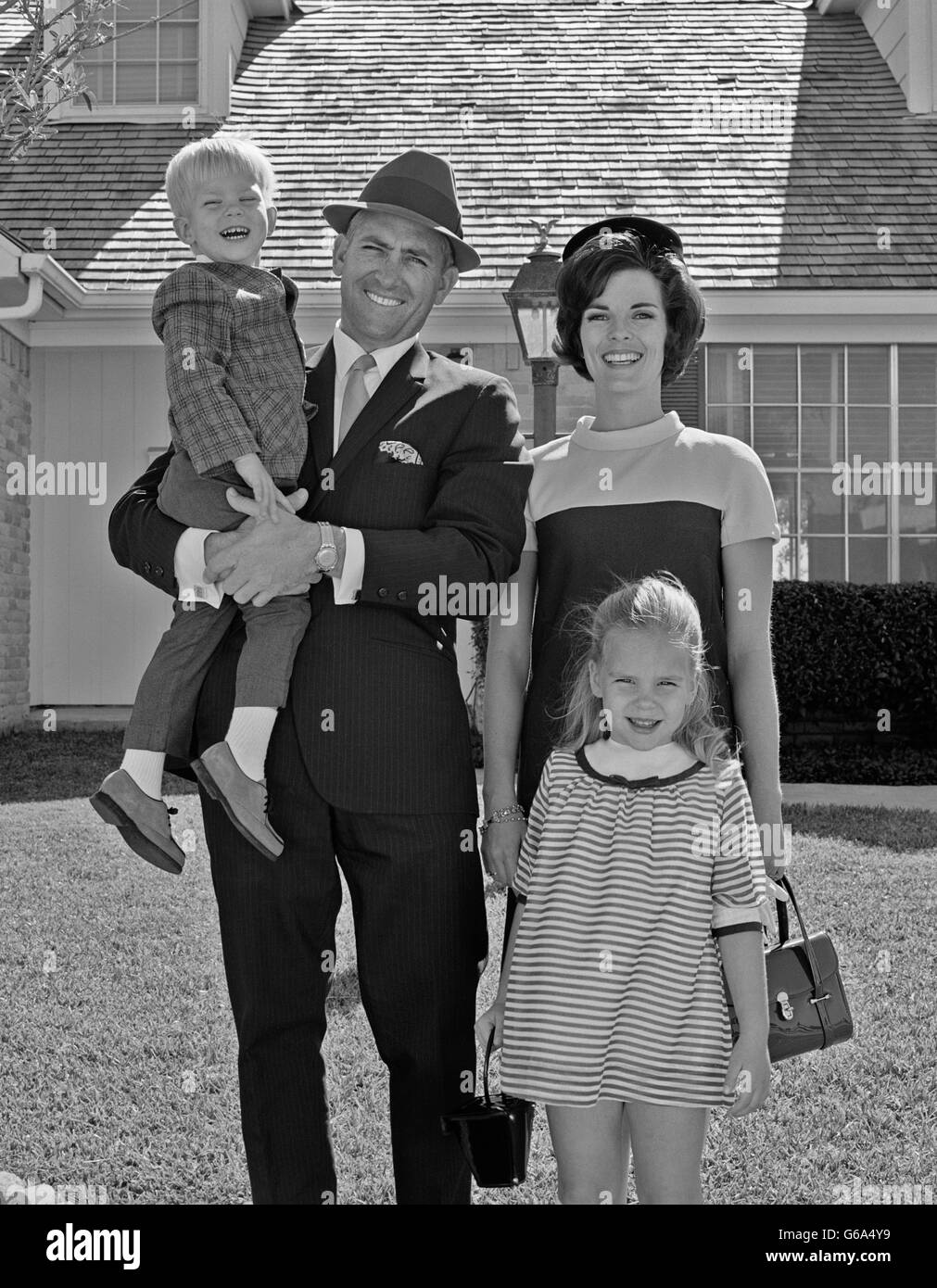 Anni sessanta ritratto sorridente madre di famiglia padre figlio permanente figlia in posa sul prato anteriore della casa suburbana guardando la fotocamera Foto Stock