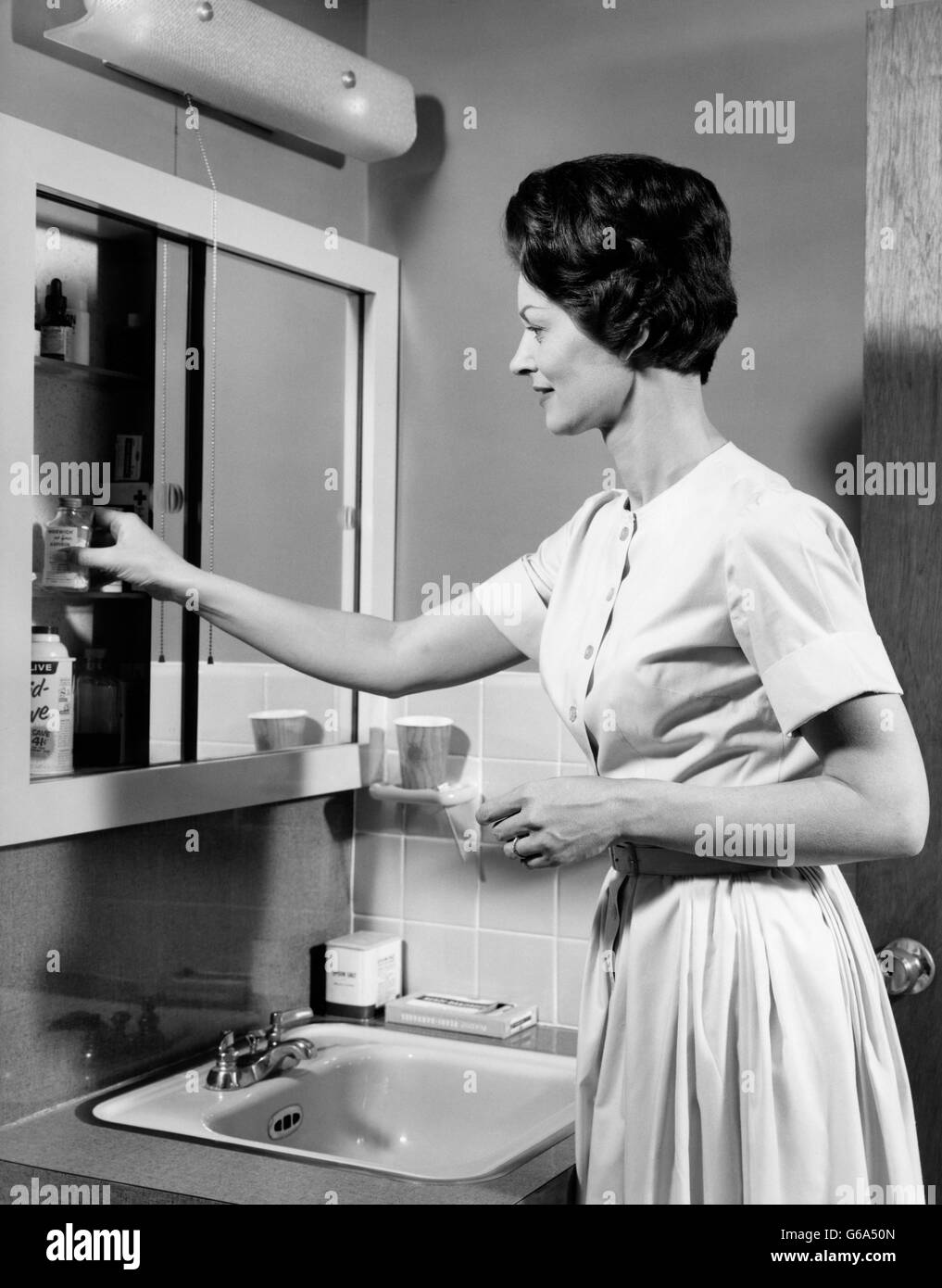 Anni sessanta BRUNETTE donna prendendo le pillole di bottiglia AL DI FUORI DEL BAGNO Armadietto dei medicinali Foto Stock