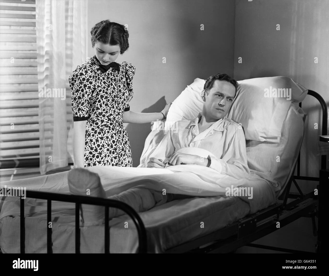 1930s donna dal posto letto uomo nel letto di ospedale premuto con gamba bendato Foto Stock