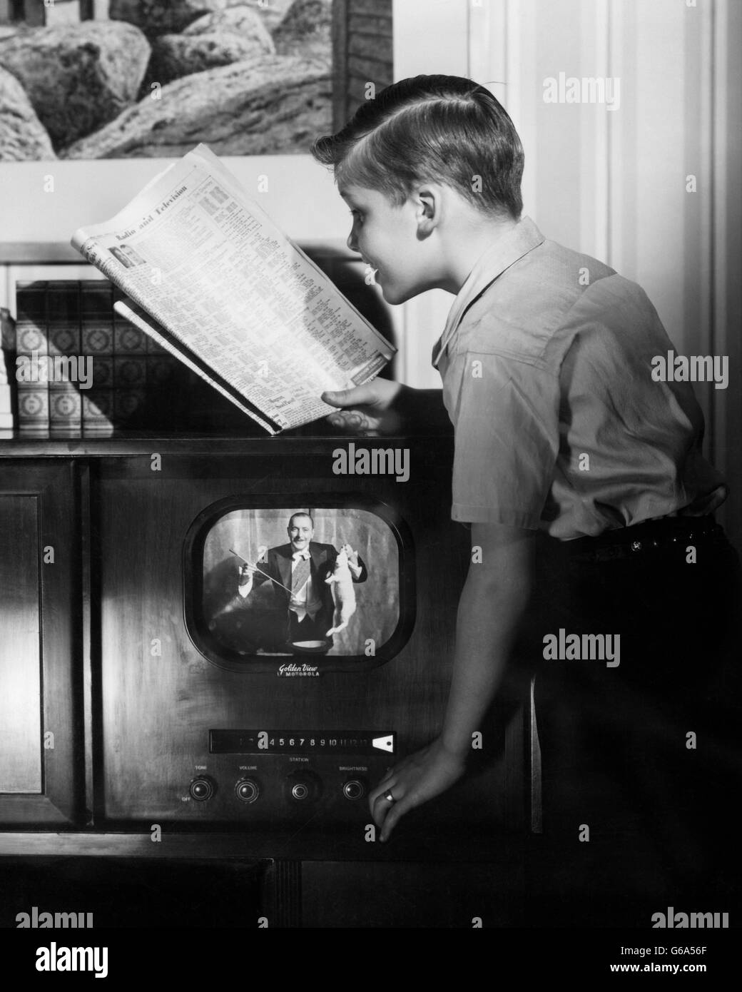 1940s ragazzo lettura giornali GUIDA TV adegua la sua televisione al canale corretto Foto Stock