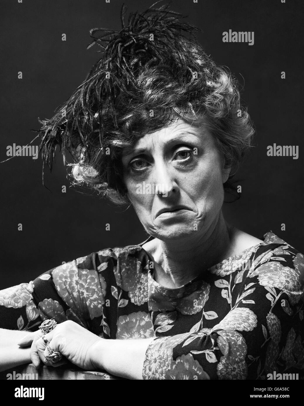 Anni Settanta ritratto di donna SENIOR CON MEDIA SOUR triste arrabbiato espressione facciale indossando un cappello piumato guardando la fotocamera Foto Stock