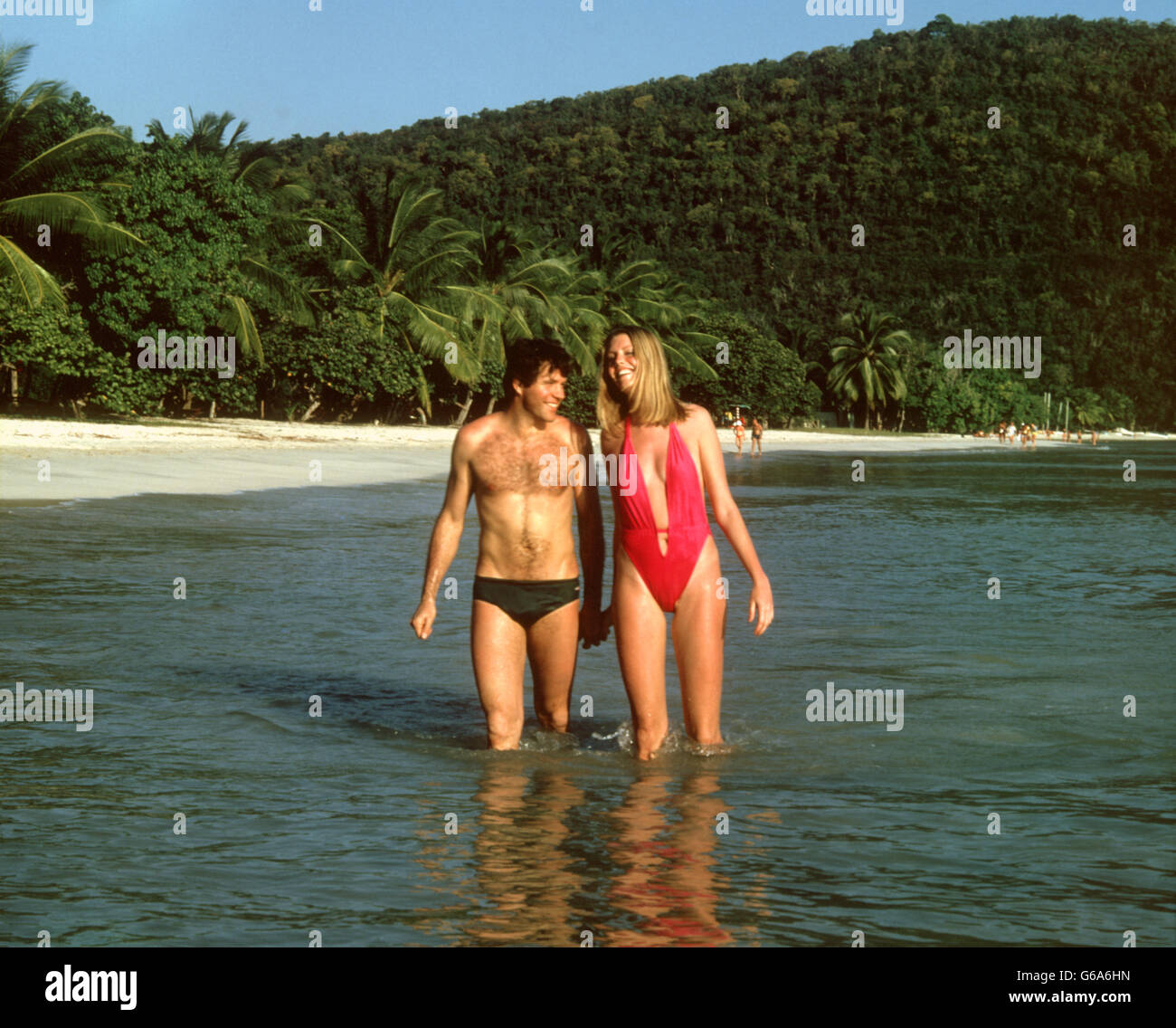 Anni Settanta anni ottanta giovane camminare insieme oceano spiaggia tropicale tenendo le mani Foto Stock