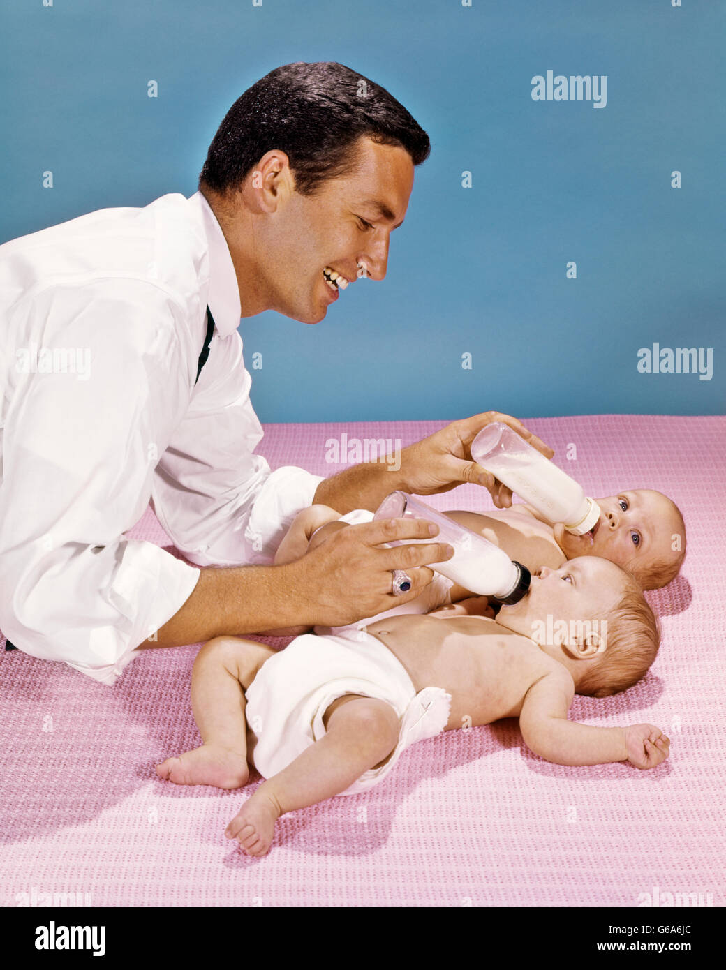 Anni sessanta Padre Gemelli di alimentazione dei neonati con flaconi contemporaneamente Foto Stock