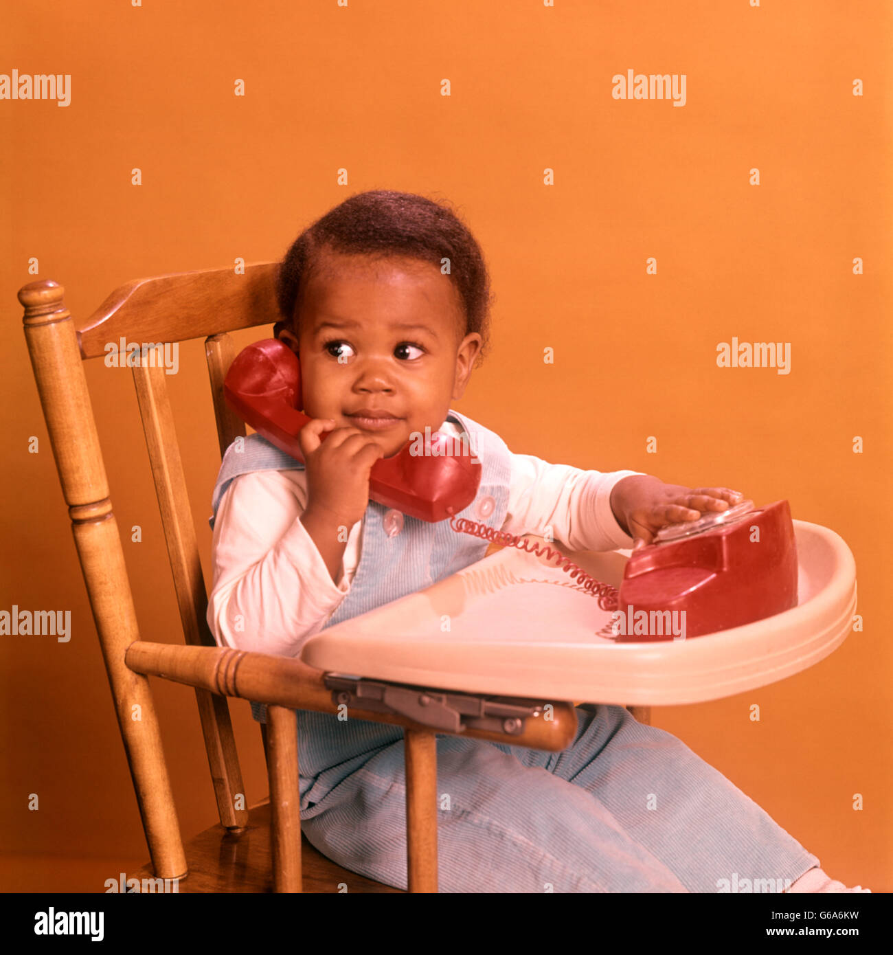 Anni Settanta African American Boy giocando con telefono GIOCATTOLO SEDUTO nel seggiolone Foto Stock