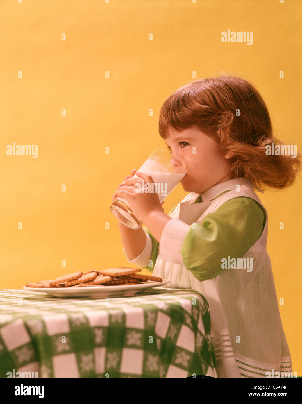 Anni Settanta anni sessanta ragazza di bere un bicchiere di latte i cookie sul tavolo Foto Stock