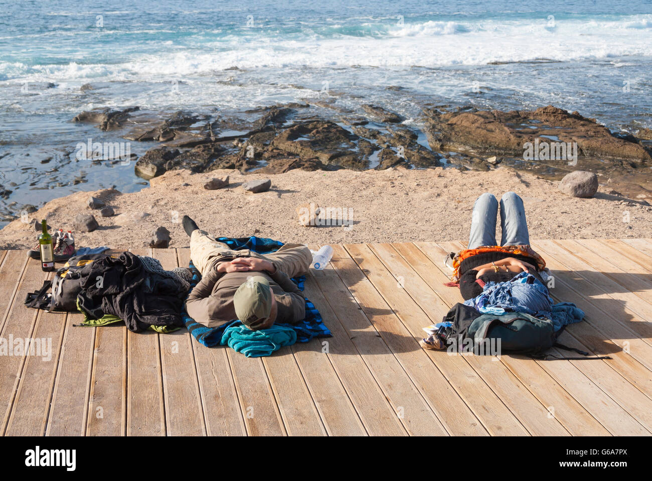 Maschio e femmina per backpackers in relax sulla passerella di legno che si affaccia sulla spiaggia di surf a Las Palmas de Gran Canaria, Isole Canarie Foto Stock