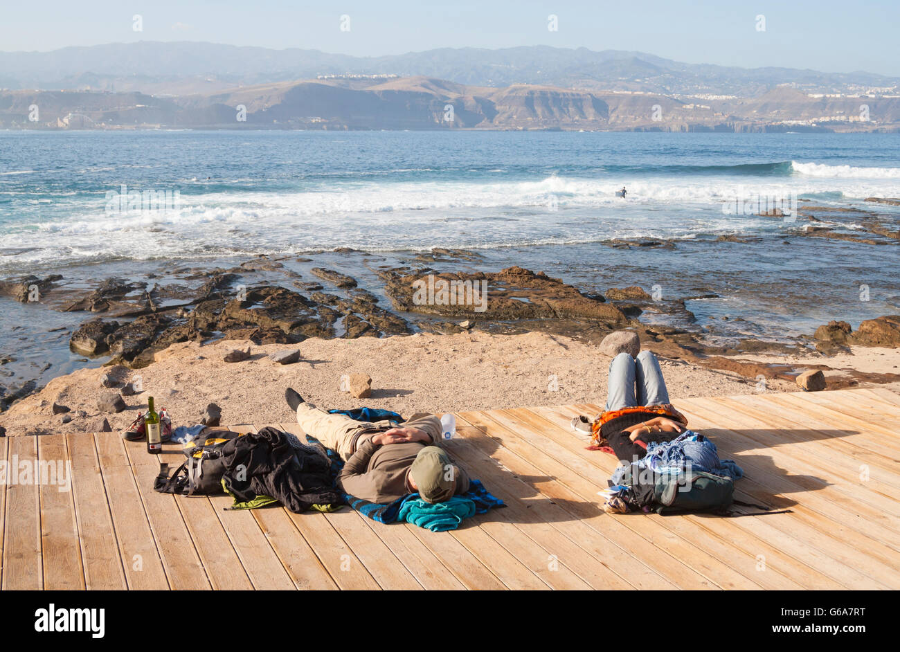 Maschio e femmina per backpackers in relax sulla passerella di legno che si affaccia sulla spiaggia di surf a Las Palmas de Gran Canaria, Isole Canarie Foto Stock