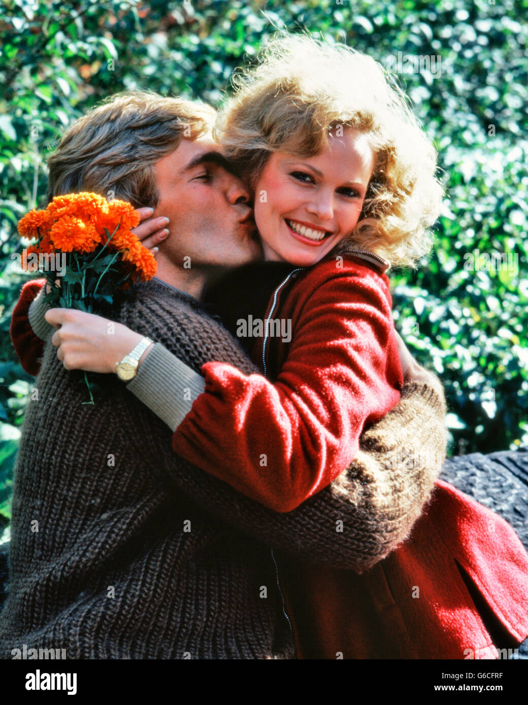 Anni ottanta sorridente giovane abbracciando ALL'APERTO DONNA HOLDING bouquet di fiori d'arancio Foto Stock
