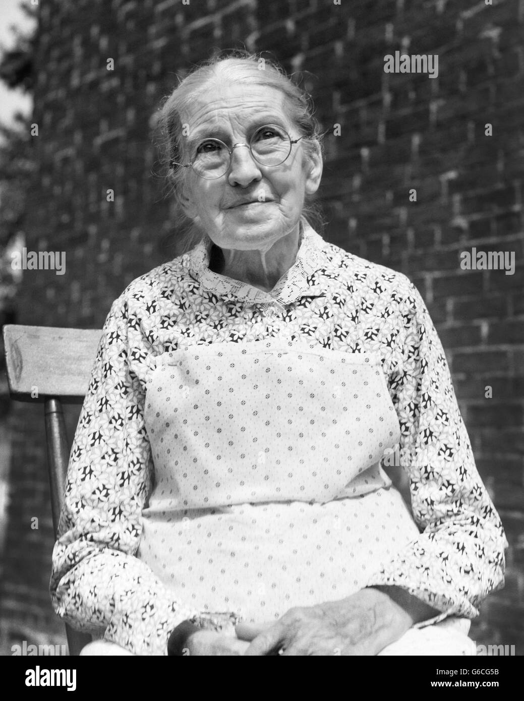 1930s ritratto donna anziana indossando occhiali abito stampa Bavaglino bianco grembiule Foto Stock