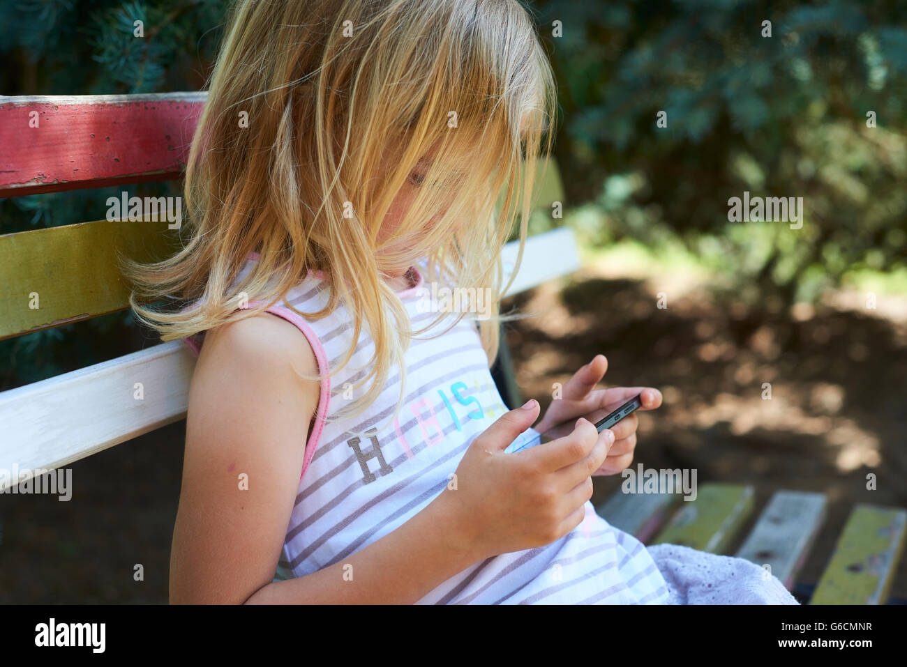 Bella bionda caucasica ragazza seduta su una vecchia panchina del parco giocando su smart phone Foto Stock