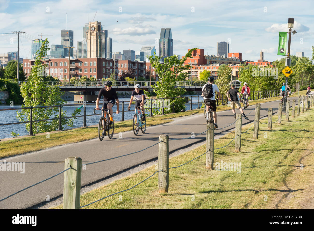 Gente in bicicletta su Lachine Canal's bike path in Montreal, con skyline in background e atwater market tower Foto Stock