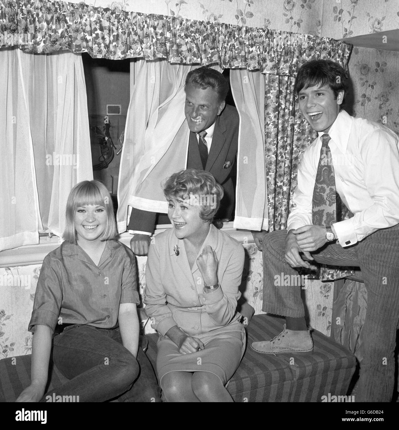 L'evangelista americano Billy Graham ha una vista dalla finestra delle stelle Ann Holloway (l), Dora Bryan e Cliff Richard durante la sua visita al set del film 'Two A Penny' presso gli studi Goldhawk, Shepherd's Bush, Londra. La star pop Cliff ha il suo primo ruolo drammatico nel film, con Dora Bryan che gioca come madre. Il dottor Graham farà un'apparizione ospite in una sequenza girata durante la sua Greater London Crusade del 1966 a Earl's Court. Foto Stock