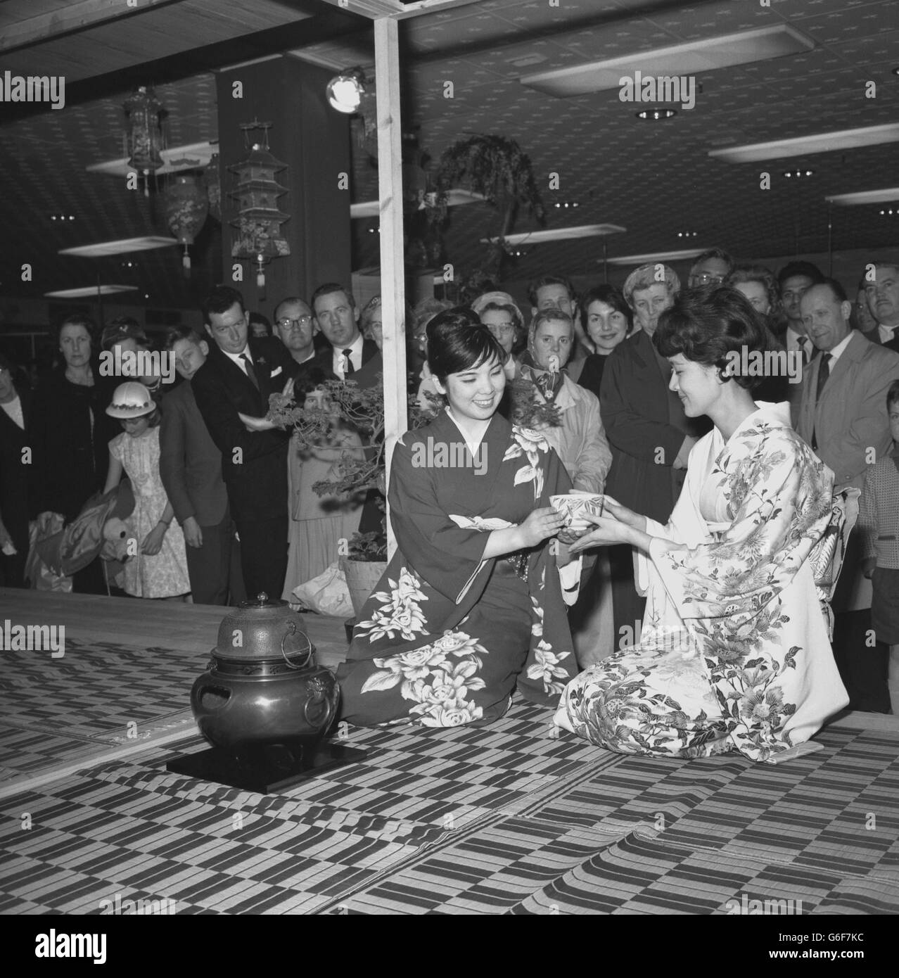 Una folla guarda le donne giapponesi rivestite di kimono la signorina Eiko Murai (a sinistra) e la signorina Mitchiko Ishikawa eseguire un'antica cerimonia di preparazione del tè presso il negozio Selfridge di Oxford Street, Londra, durante una settimana di mostra di prodotti giapponesi. Il rituale per la preparazione del tè è considerato un promotore della compostezza mentale. Foto Stock