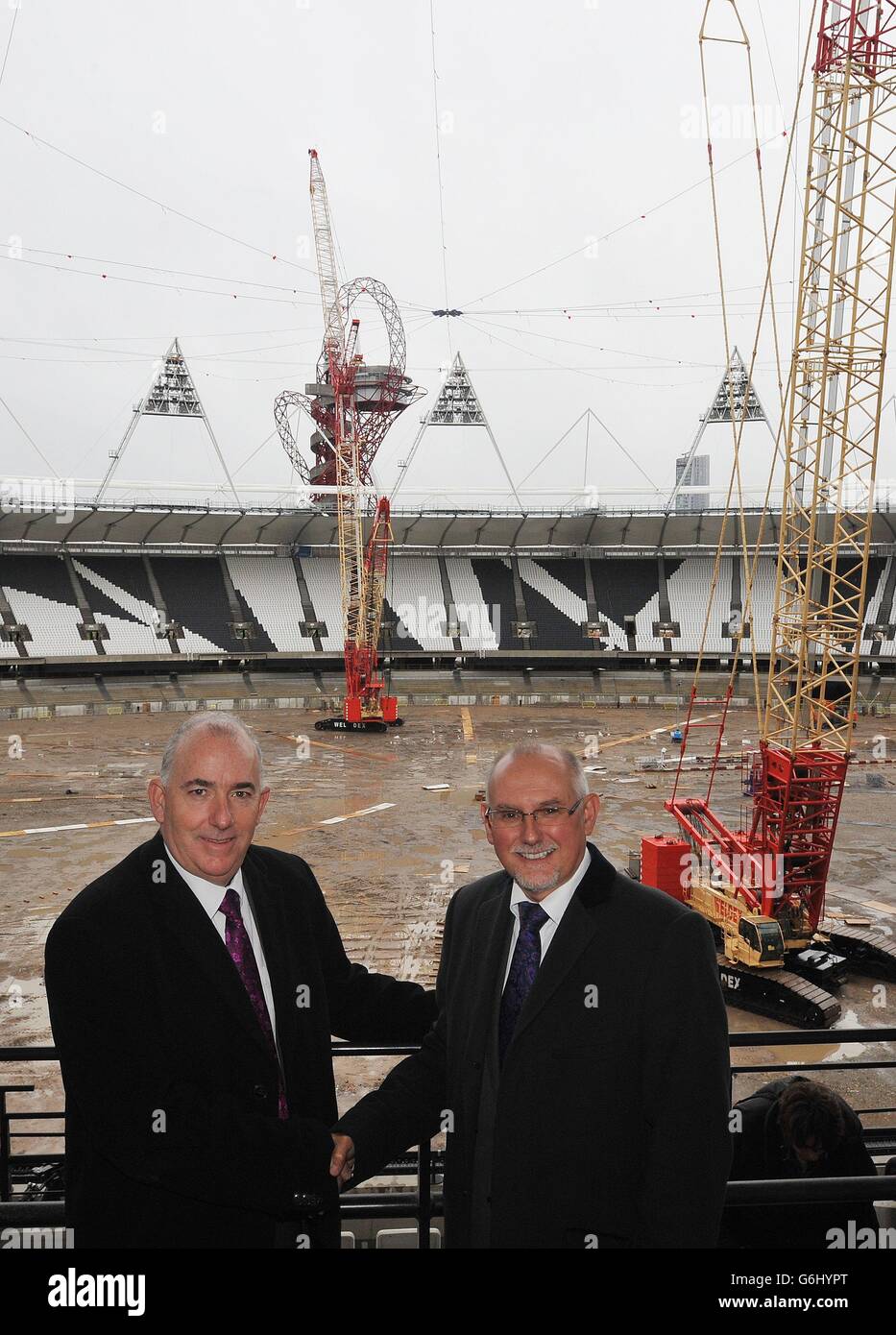 Kim Bromley-Derry (a sinistra), amministratore delegato del consiglio di Newham, scrolla le mani con Dennis Hone, amministratore delegato della London Legacy Development Corporation, mentre le gru per sollevamento pesante si trovano in folle al Queen Elizabeth Olympic Park Stadium, a Stratford, nella zona est di Londra, dopo che le condizioni meteorologiche hanno ritardato la rimozione dei primi pannelli luminosi, Mentre il lavoro inizia a trasformarsi in un luogo multiuso aperto tutto l'anno e sede permanente del West Ham United Football Club e del nuovo stadio nazionale di competizione per gli atleti del Regno Unito. Foto Stock