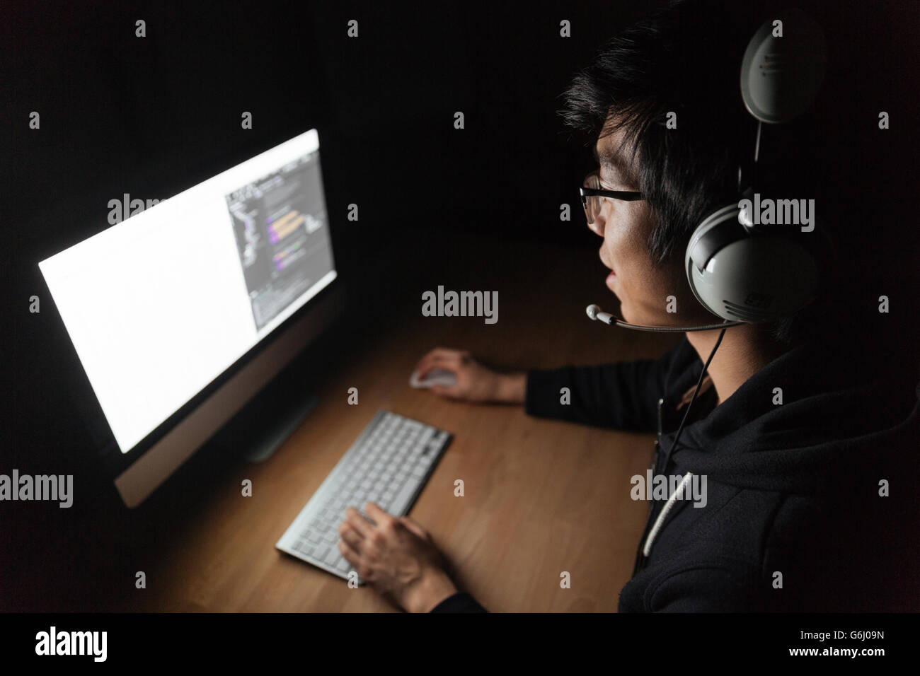 Concentrato maschio asiatici gamer seduta e la riproduzione di giochi per computer in camera oscura Foto Stock