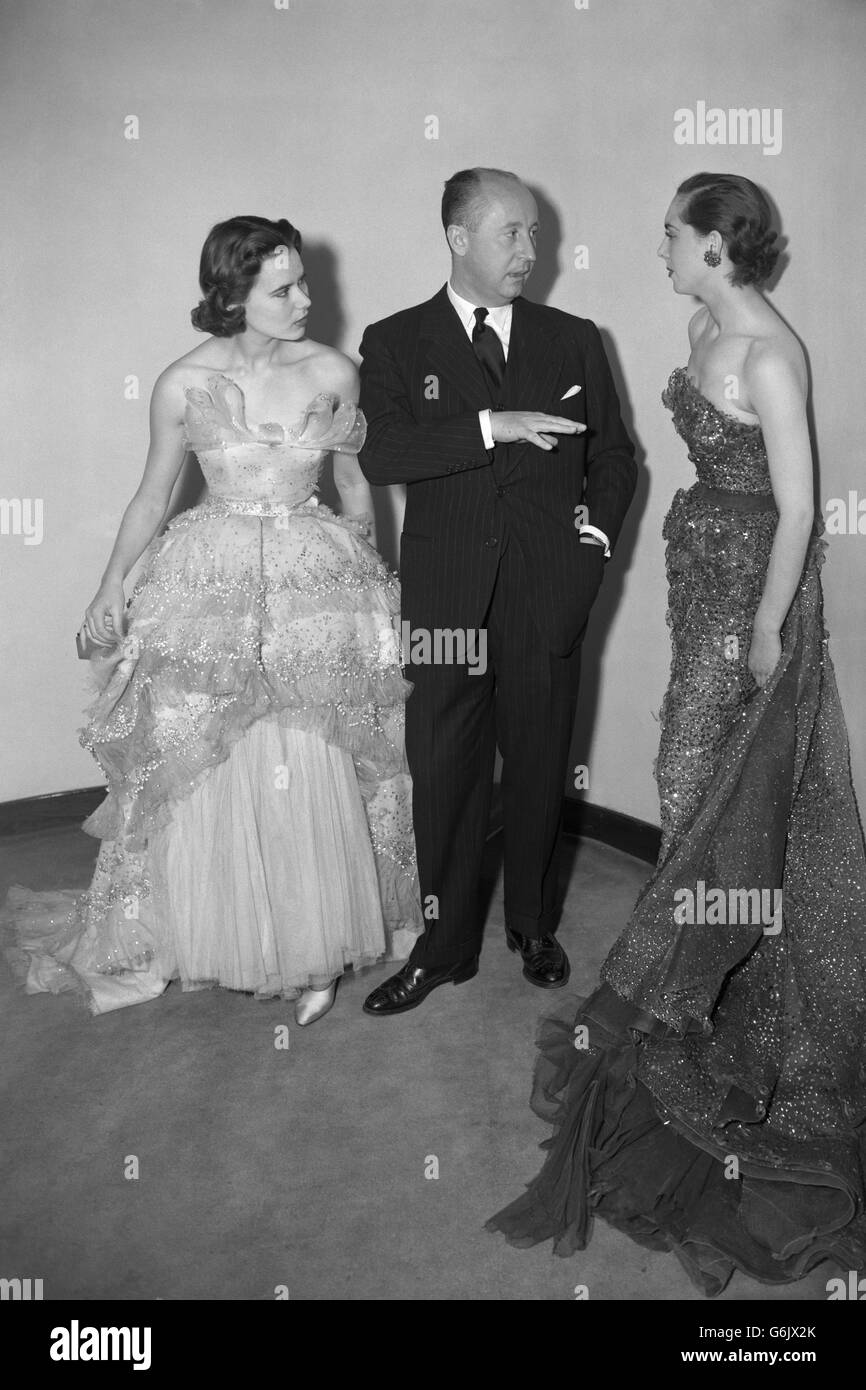 Il famoso designer francese Christian Dior, esteso a mano, sottolinea un  punto di moda mentre parla con due dei suoi modelli alla sfilata di moda  del Savoy Hotel di Londra. L'abito sulla