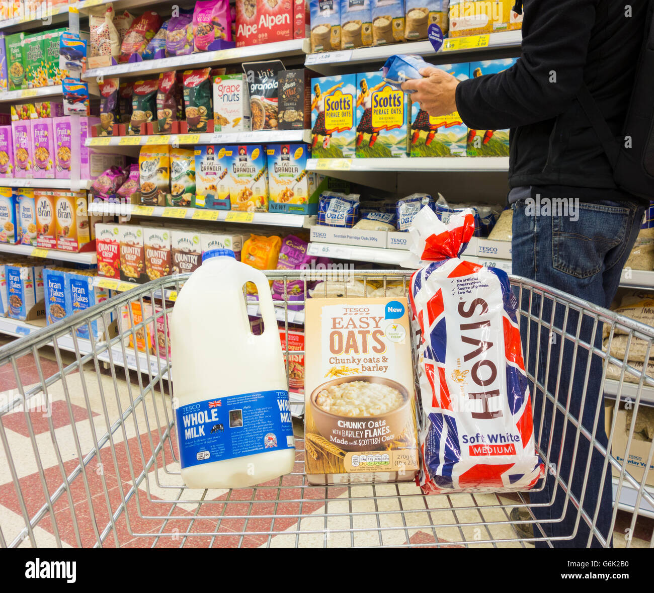 Uomo con latte, pane e porridge avena nel carrello della spesa al supermercato Tesco. REGNO UNITO. Aumento dei prezzi alimentari... Foto Stock