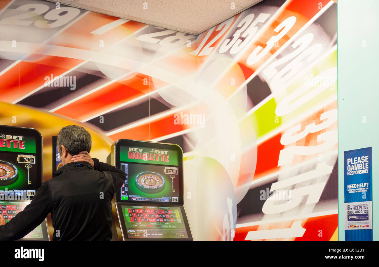 Uomo maturo con quote fisse della macchina di scommesse in bookmakers. Inghilterra, Regno Unito. Foto Stock
