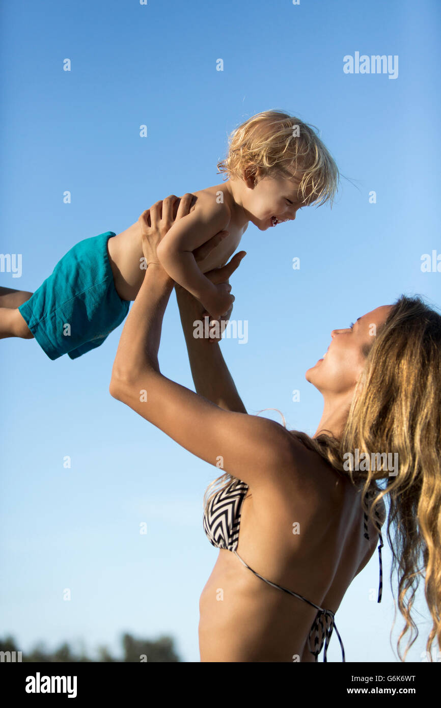 Felice madre in bikini sollevando il suo figlio Foto Stock
