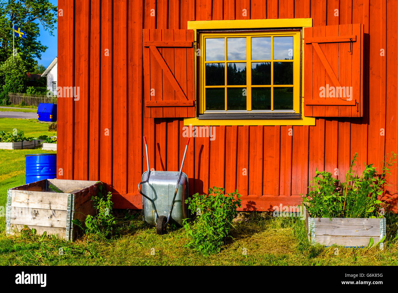 Molto colorato, edificio rosso con carriola e spalliere di palette utilizzati come sollevata letti di giardinaggio di fronte ad esso. Finestra di colore giallo con Foto Stock