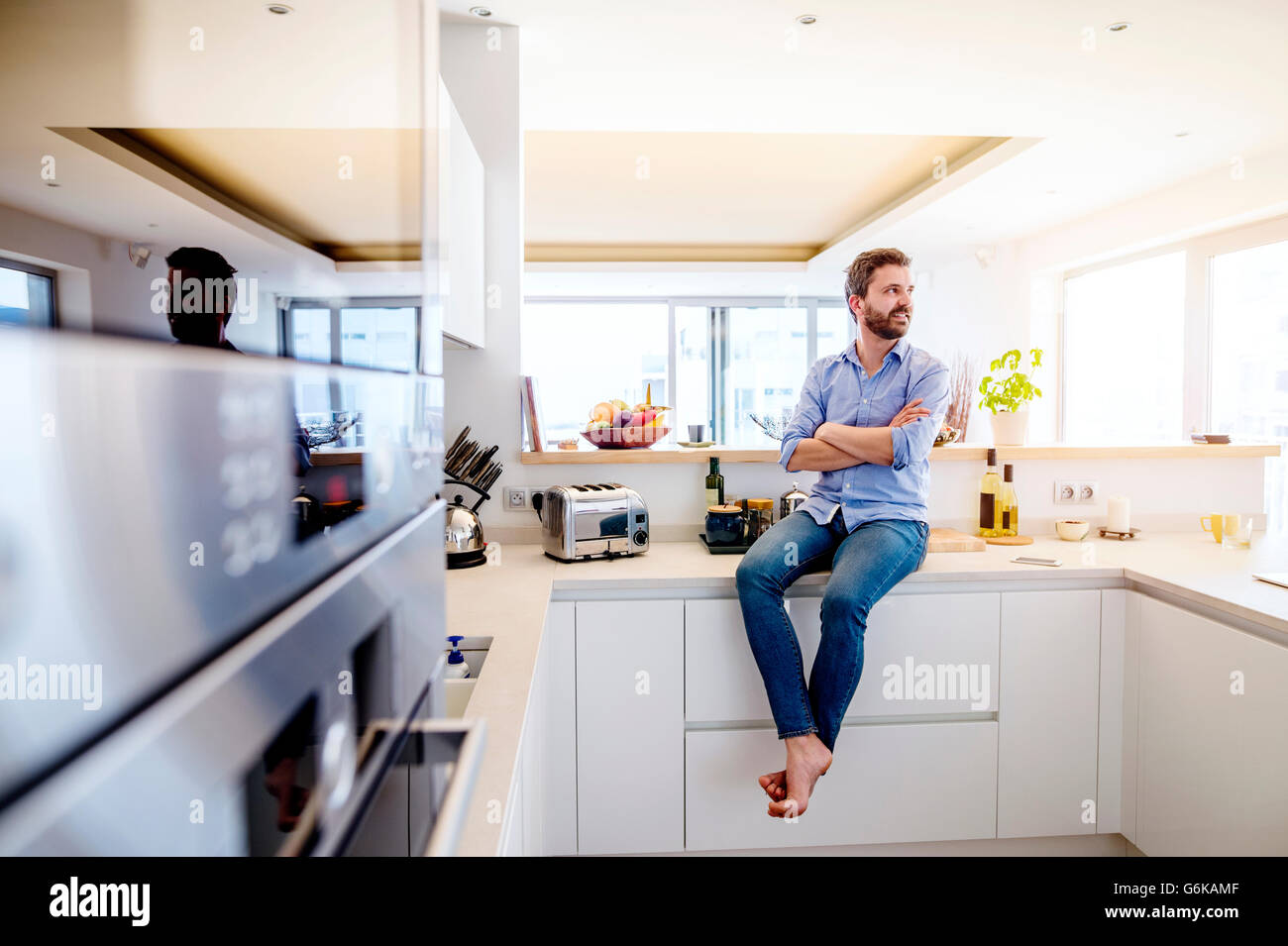 Uomo seduto in cucina con le braccia incrociate Foto Stock
