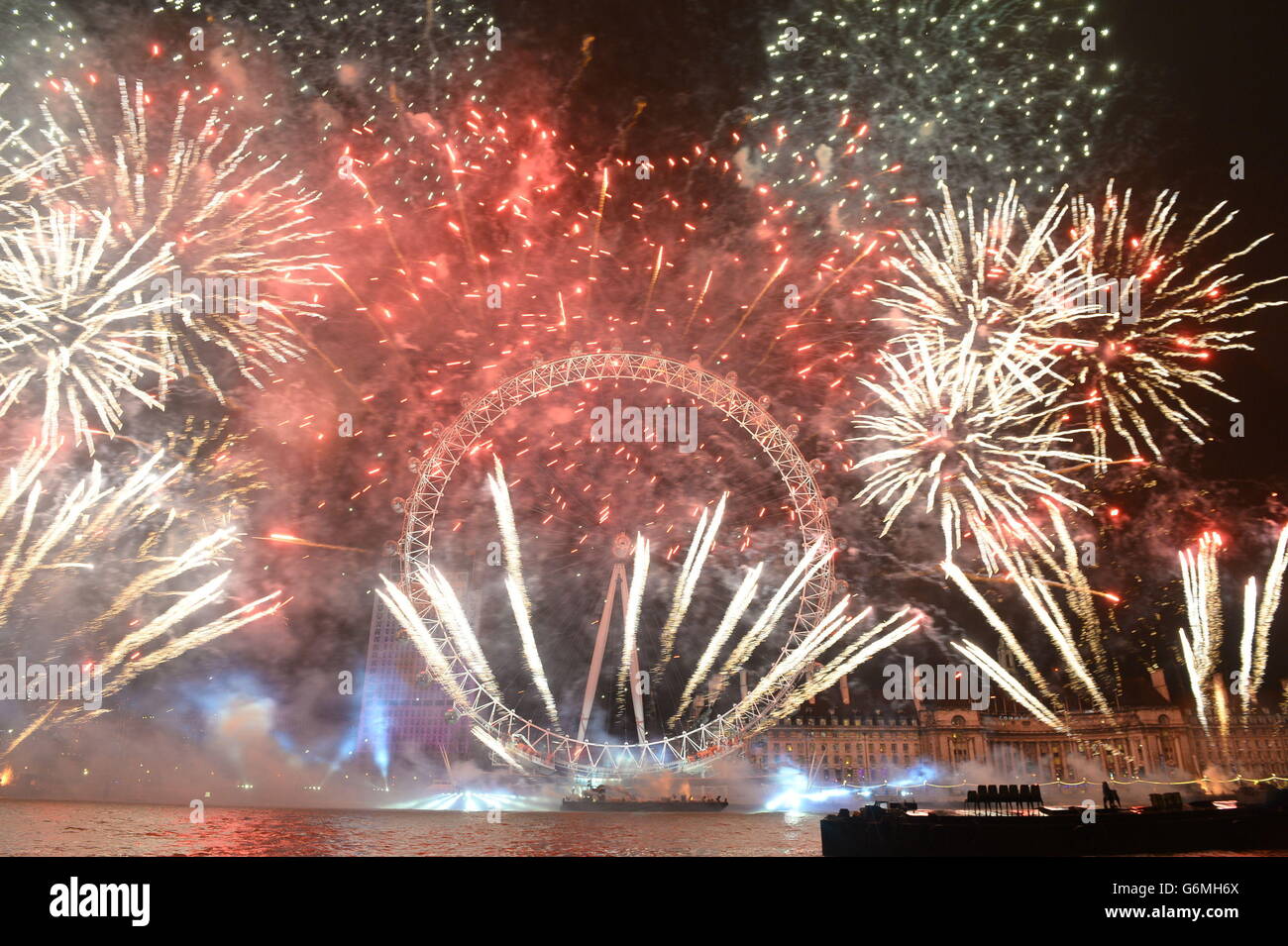 Fuochi d'artificio illuminano il cielo sopra il London Eye a Londra centrale durante i festeggiamenti di Capodanno. Foto Stock