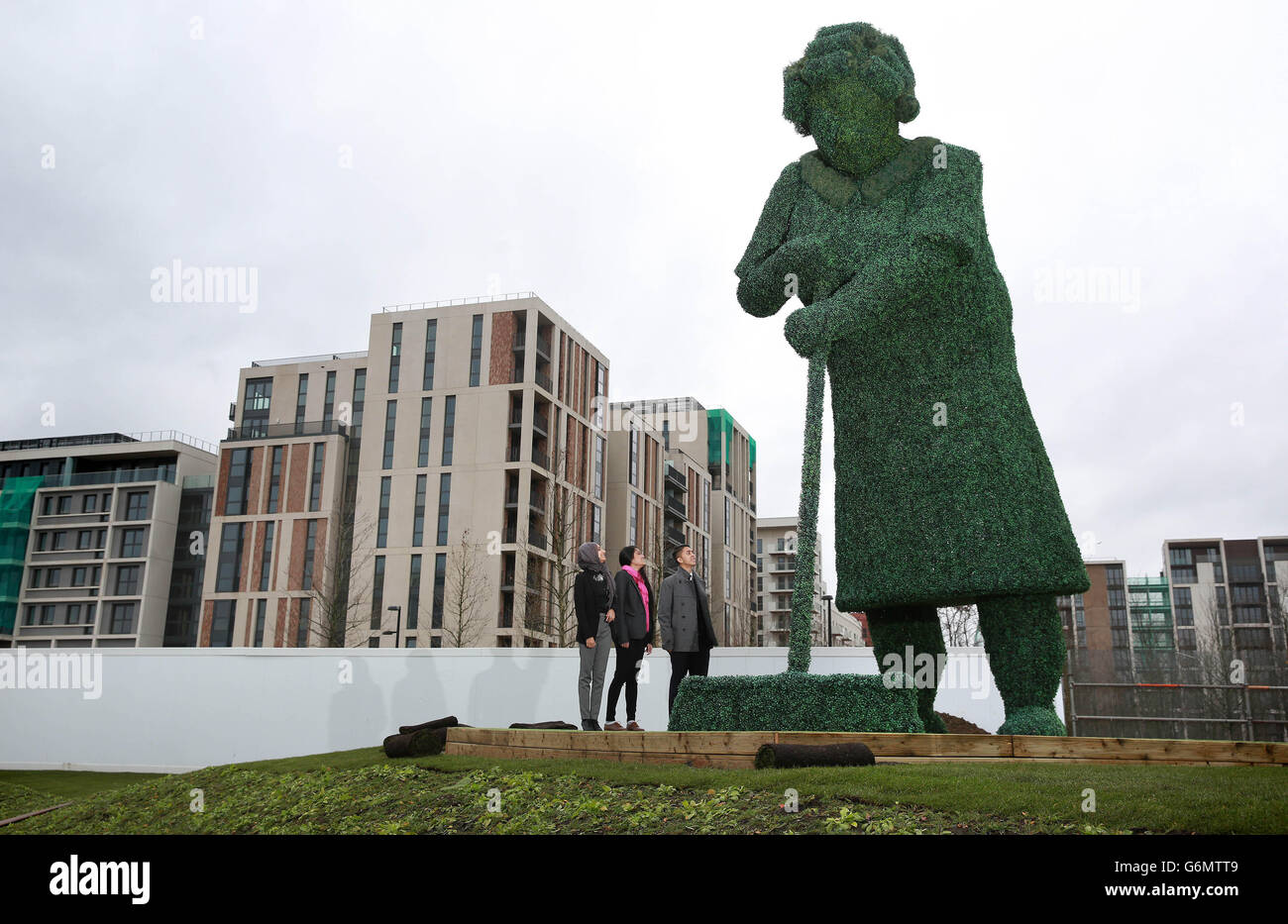 (Da sinistra a destra) Juned Uddin, 16, Aniqa Begum, 17, E Nazeen Patel, 17, dalla Chobham Academy guarda una delle due sculture topiarie alte 20 piedi, chiamata 'Old Woman' fatta da Shipshape Arts, come va in mostra nell'East Village, il quartiere più nuovo di Londra costruito sul luogo dell'ex Villaggio Olimpico e Paralimpico nella parte est di Londra. Foto Stock