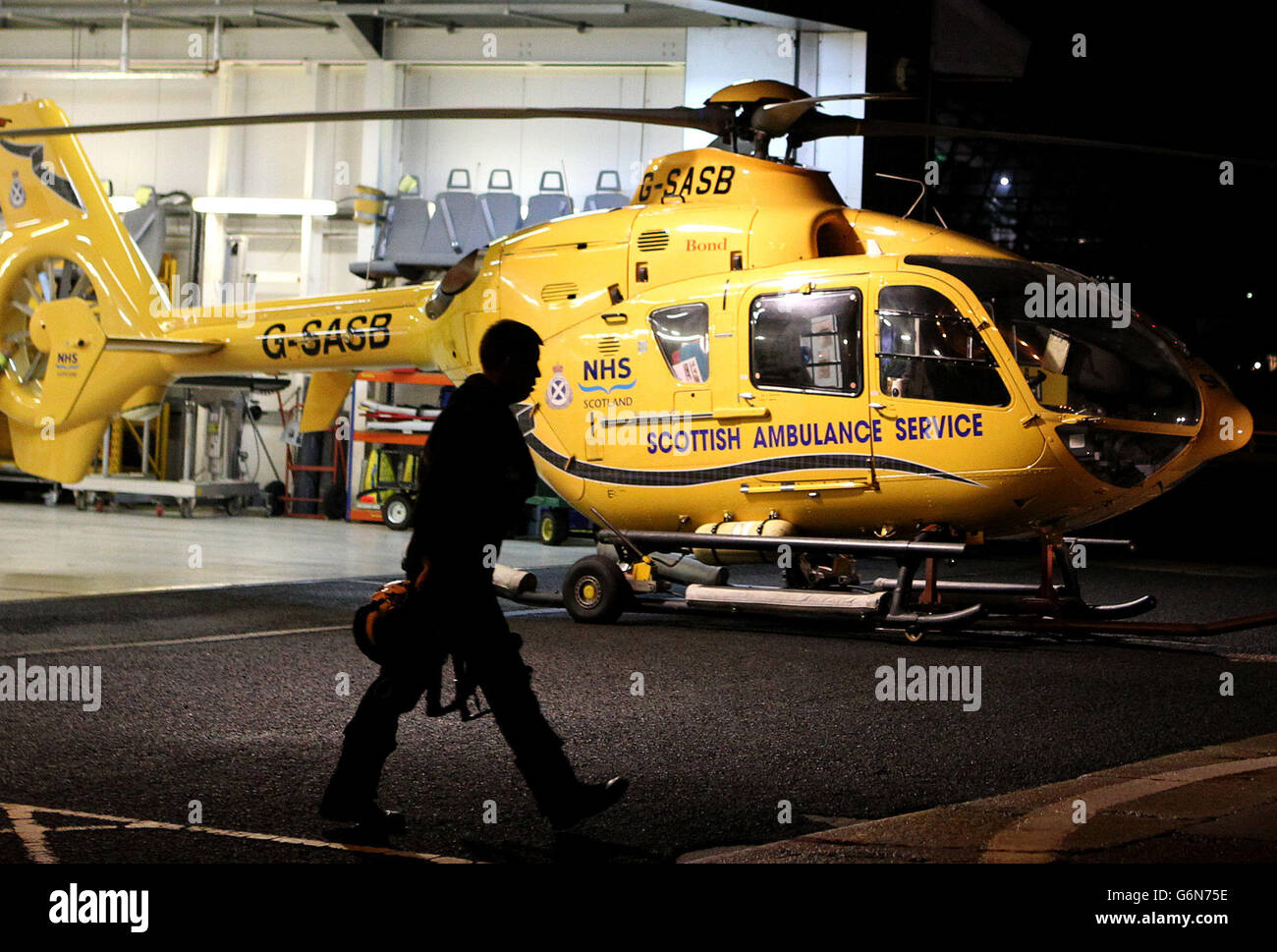 Un pilota passa accanto a un elicottero Scottish Ambulance Service nel suo hangar alla sua base presso l'eliporto di Glasgow City sul fiume Clyde dopo, restrizioni ereditate da Bond sulla polizia Scozia e gli elicotteri Scottish Ambulance Service. Foto Stock