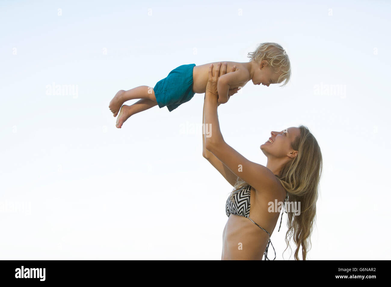 Felice madre in bikini sollevando il suo figlio Foto Stock