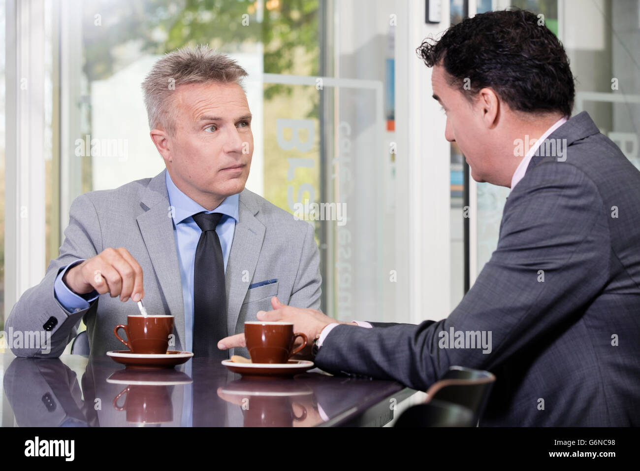 Due fiduciosi e gli imprenditori di successo parlando in un grande ufficio cooperano, potrebbe essere client consigli con caffè Foto Stock