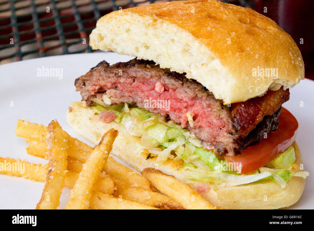 Hamburger alla griglia con pancetta, shredded lattuga, fetta di pomodoro. Carne sul pane con patate fritte su outdoor, ferro battuto Foto Stock