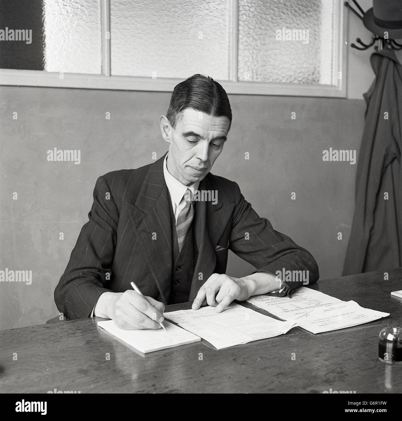 Degli anni Cinquanta, storico, un senior manager o executive in industria britannica nel suo ufficio sparse lavorando alla sua scrivania. Foto Stock