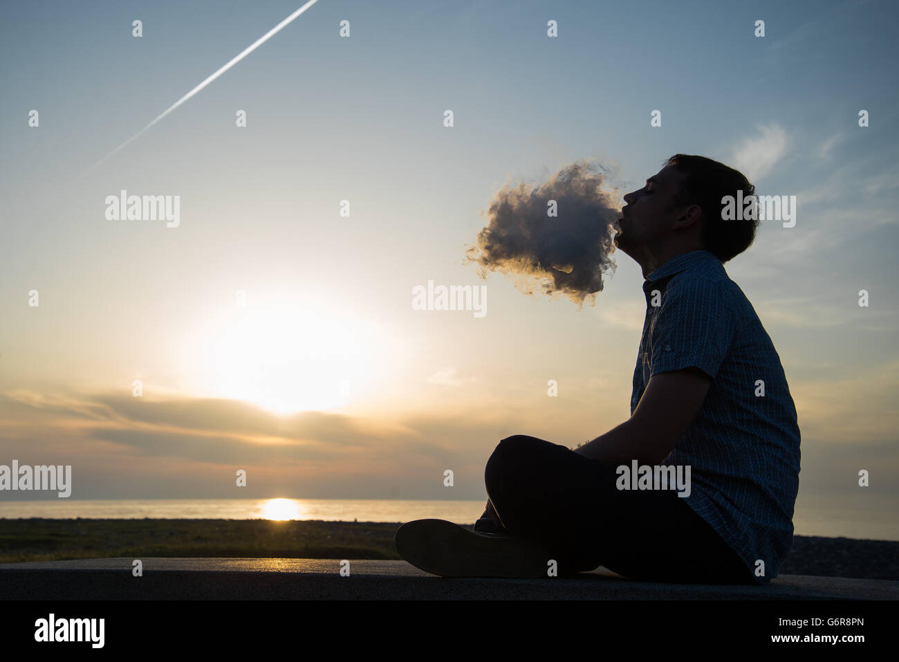 Silhouette di uomo di fumare un tubo nel cappuccio al tramonto. Fotografo in un cappello da baseball di fumare un tubo al tramonto sul mare.Travel, avventura, meditazione e rilassamento, vacanza. Foto Stock