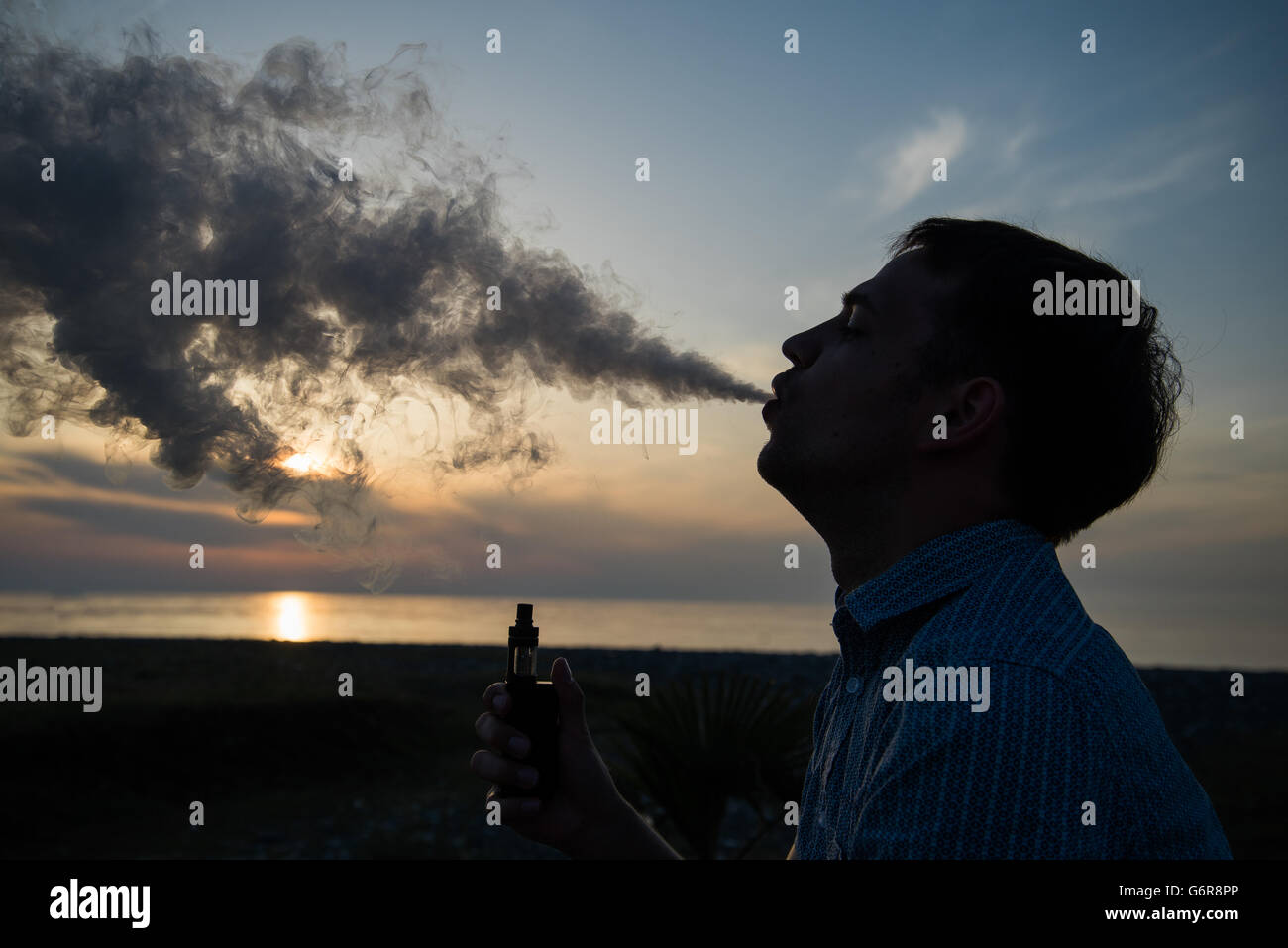 Uomo di fumare vaping e-sigaretta vape la modalità casella su GOLDEN SUNSET Foto Stock