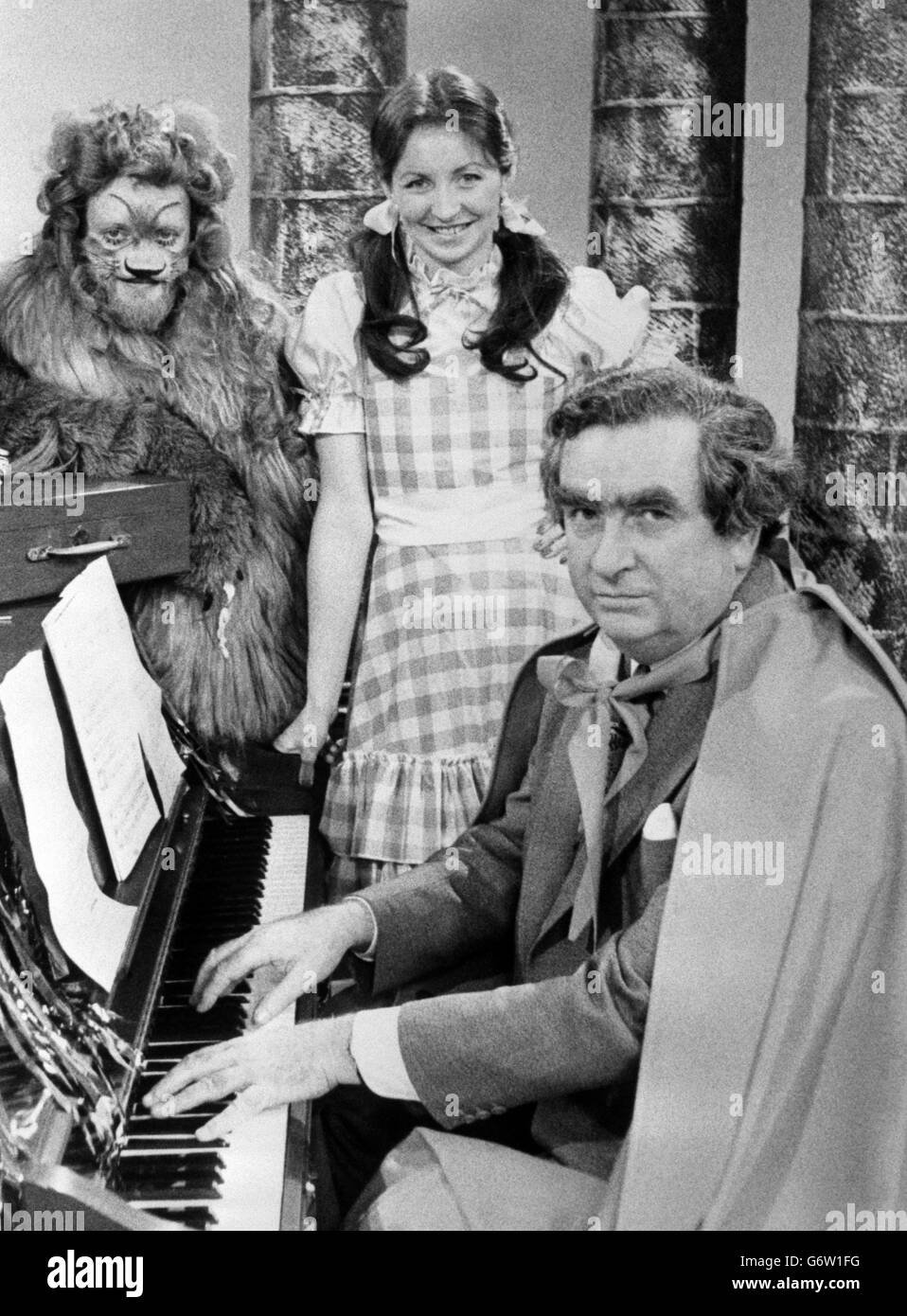 Cancelliere dello scacchiere Denis Healey (al piano) accanto ai relatori di Nationwide sue Lawley, nel vecchio ruolo di Judy Garland come Dorothy, e Richard Stilgoe, come vigliacco leone, durante le prove per la versione di Nationwide del 'Mago di Oz', da trasmettere su BBC One. In questa scena, posta al tornello del castello del mago, prima che Dorothy e i suoi amici possano passare, il Cancelliere, che è vestito e giocando 'sopra l'arcobaleno' con una scatola rossa appollaiata al pianoforte, chiede un contributo al FMI - il Fondo Internazionale dei Maghi. Foto Stock