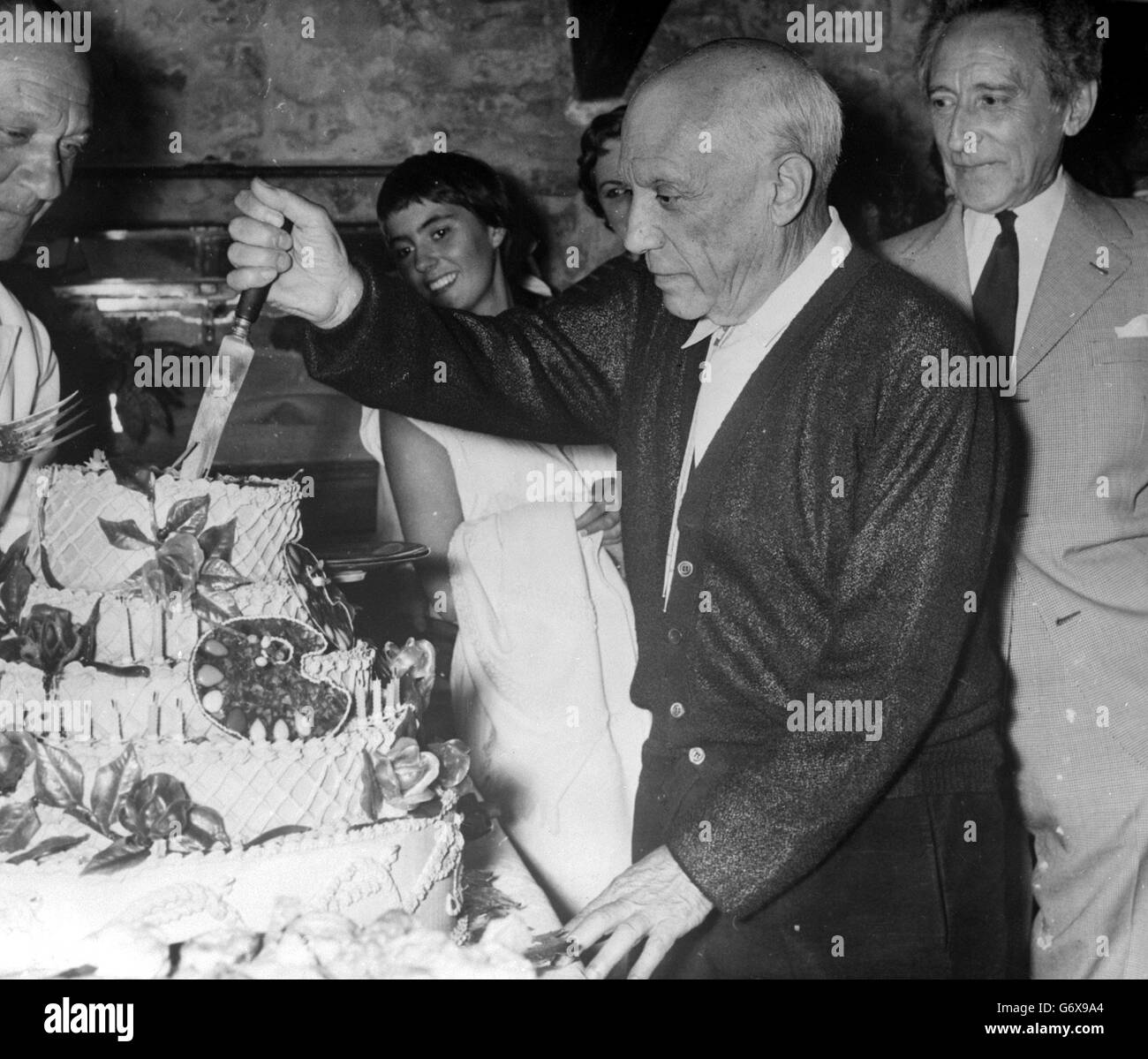 L'artista spagnolo Pablo Picasso immerge il coltello in una torta sostanziosa, decorata con tavolette, durante le celebrazioni del suo 75° compleanno a casa sua a Vallauris. A destra, dietro Picasso, è il suo amico, il poeta e drammaturgo francese Jean Cocteau. Picasso fu ospite d'onore di una festa data dai vasai di Vallauris in onore dei suoi successi, e della fama e della prosperità che ha acquistato a Vallauris. Foto Stock