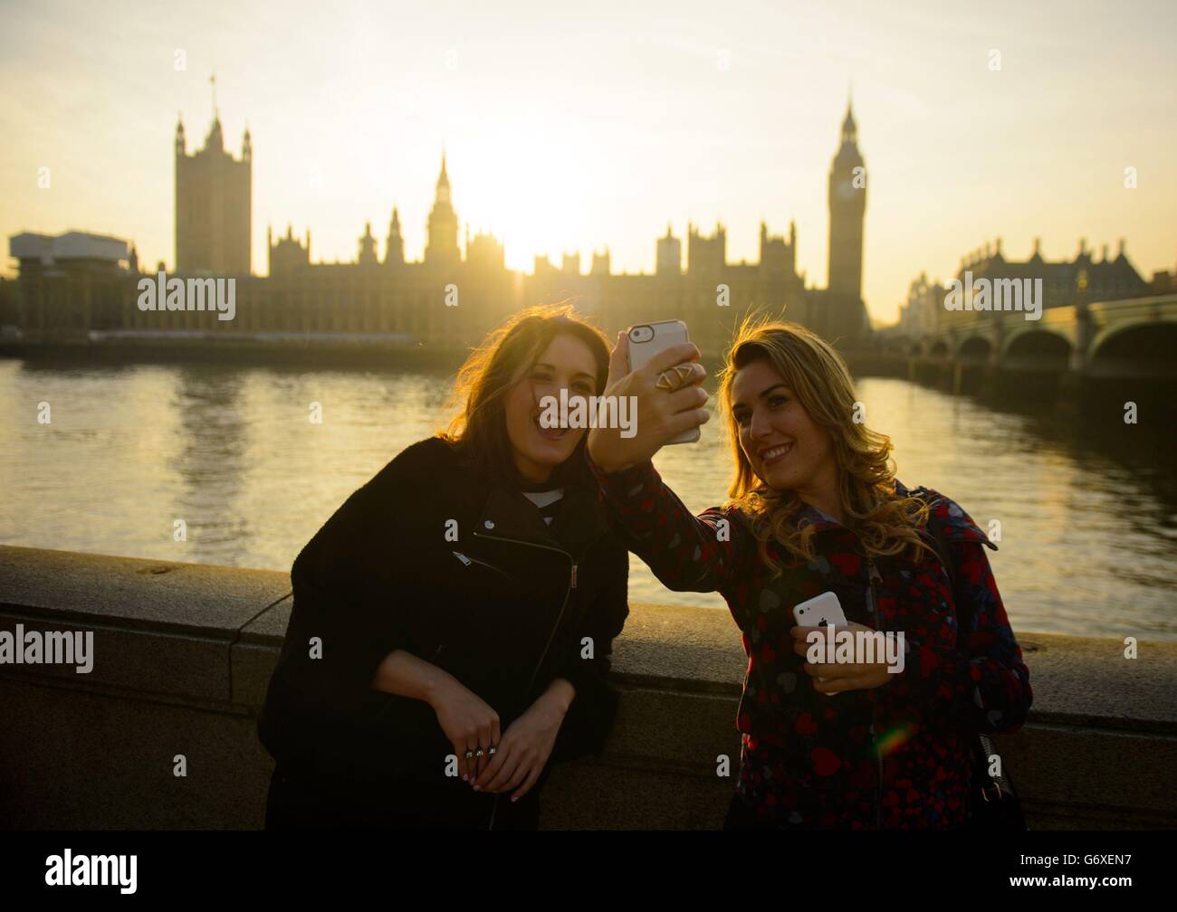 I turisti scattano una foto mentre il sole tramonta dietro le Camere del Parlamento, a Westminster, nel centro di Londra. Foto Stock