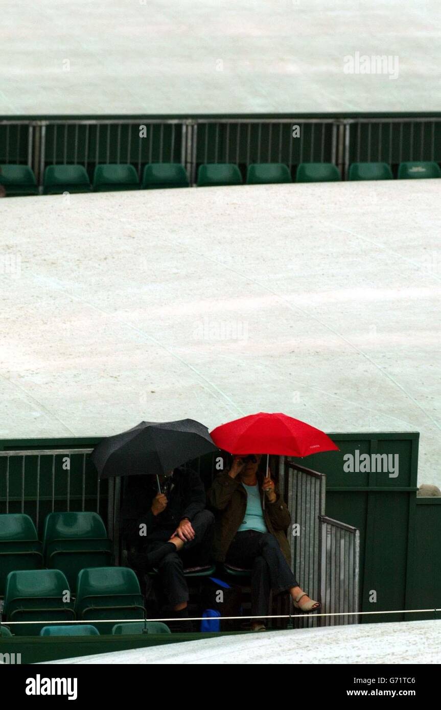 Una coppia si siede sui campi esterni in attesa della pioggia per fermarsi al Lawn Tennis Championships a Wimbledon, dove l'inizio del gioco è stato ritardato a causa delle docce. , NESSUN UTILIZZO DEL TELEFONO CELLULARE Foto Stock