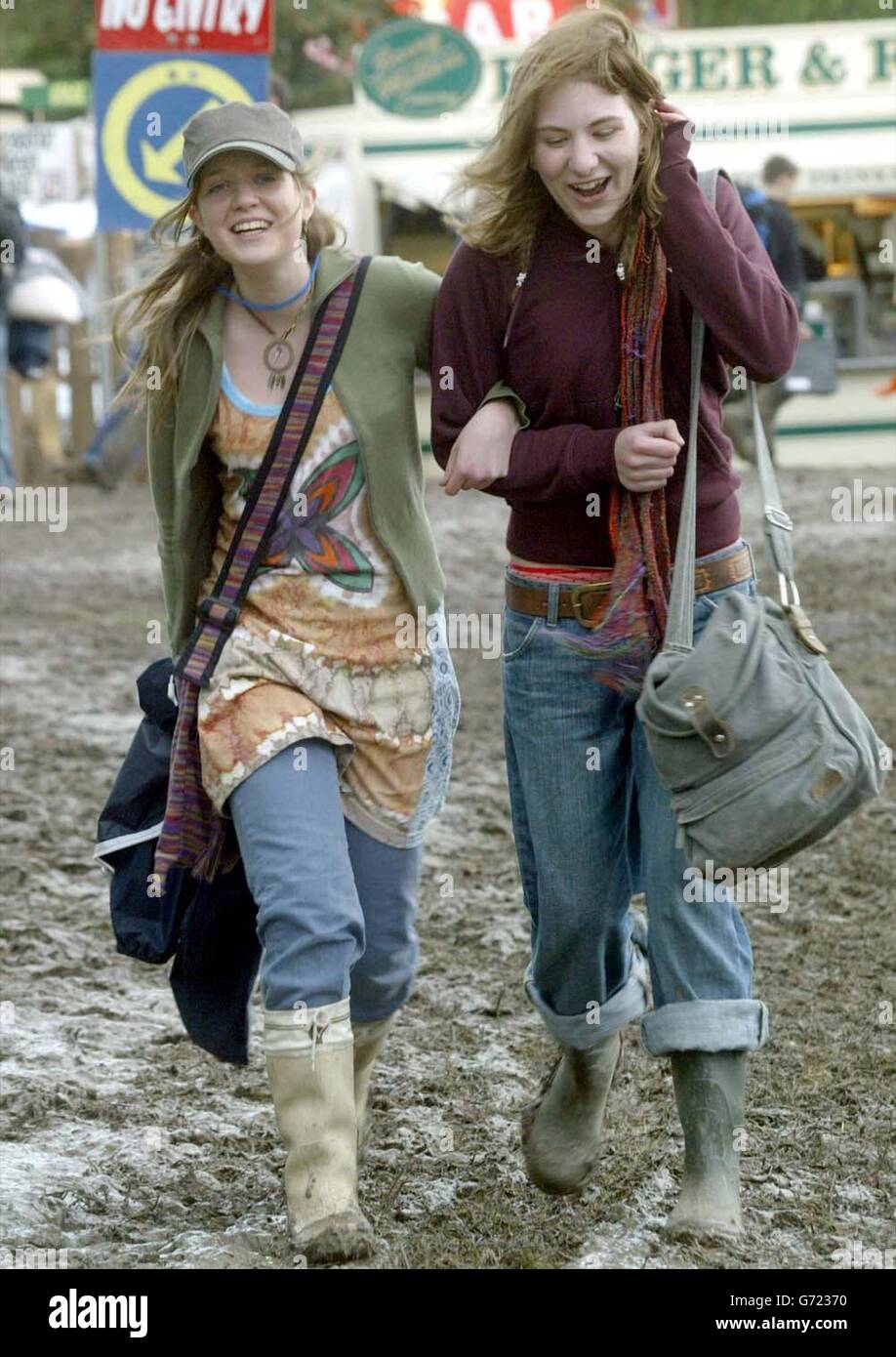 Katie May (a sinistra) e Lawrie Balsh camminano attraverso il fango presso Worthy Farm, Pilton, Somerset mentre il sito si prepara per il Glastonbury Festival 2004. Foto Stock