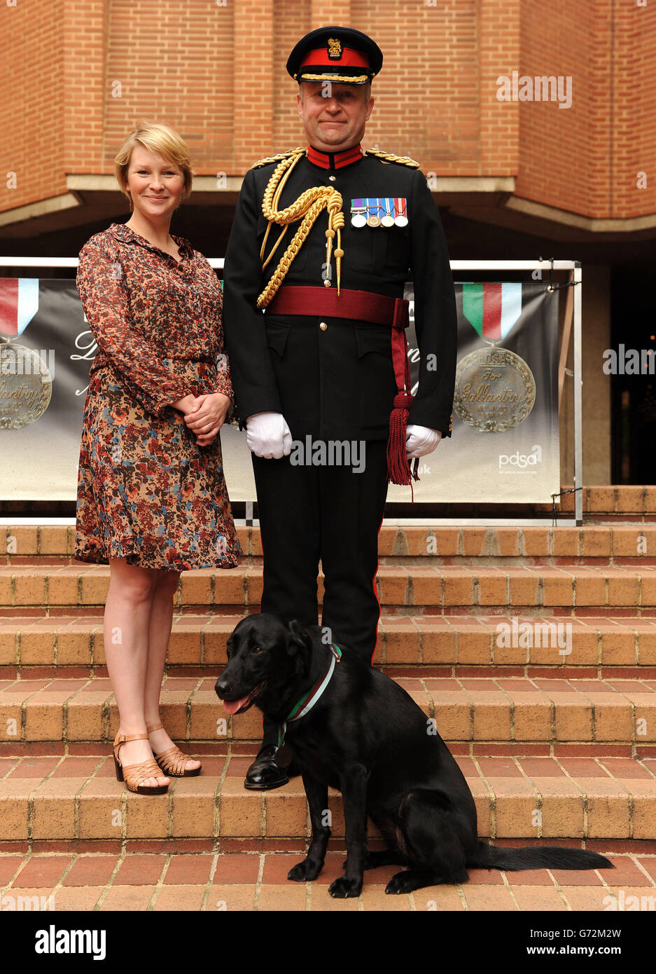 Il sergente maggiore Andy Dodds (a destra) e l'ambasciatore della PDSA Joanna Page con il cane da lavoro dell'esercito in pensione fuoco mentre indossa una replica della medaglia di Dickin della PDSA per il gallantry animale che è stato postumo assegnato al cane da lavoro militare Sasha che è stato ucciso in Afghanistan, durante un ricevimento a Londra occidentale. Foto Stock