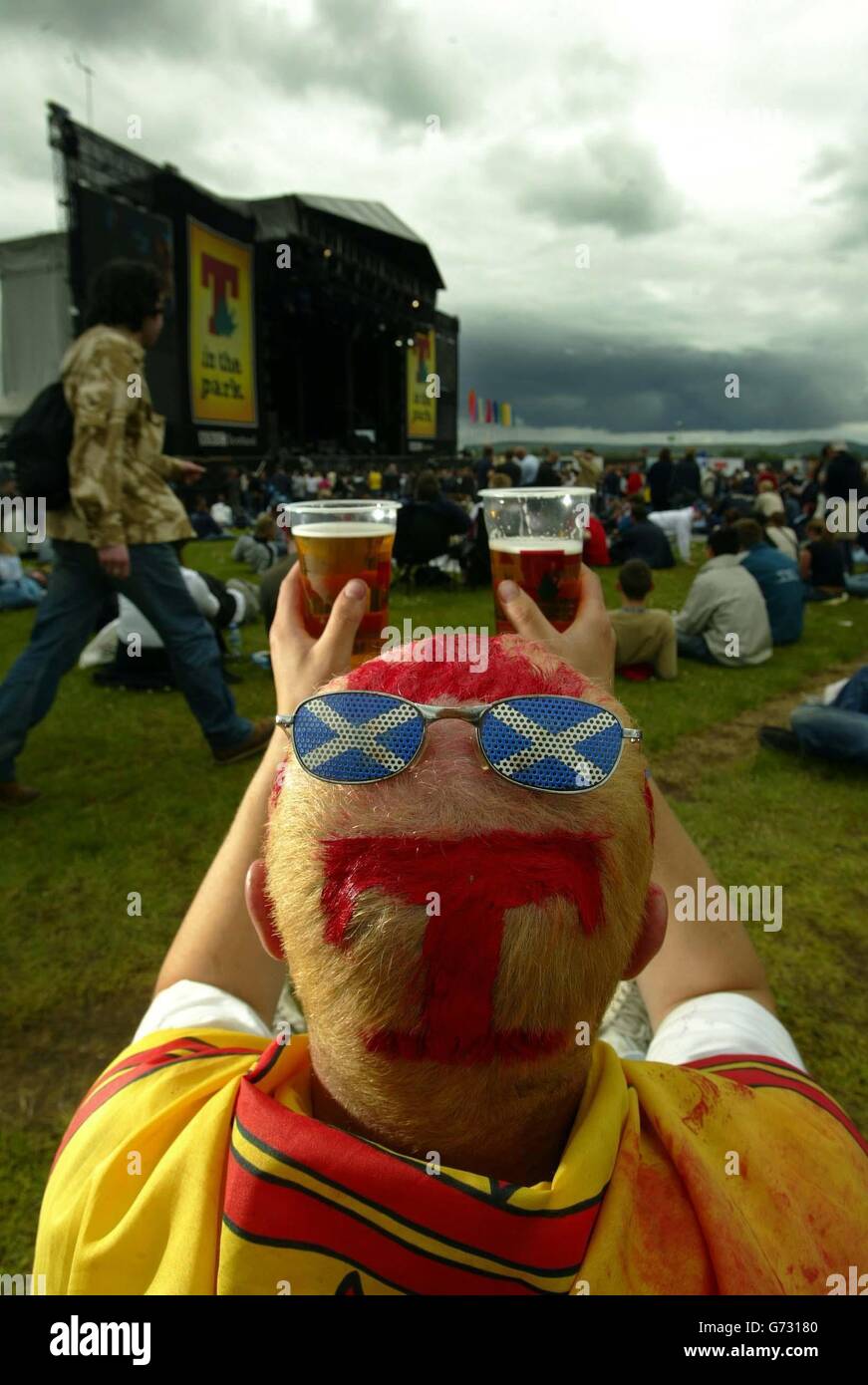 Un festaiolo dipinto con il logo T-in the Park che guarda al palco principale durante l'evento del festival musicale di due giorni a Balado, vicino a Stirling. Foto Stock