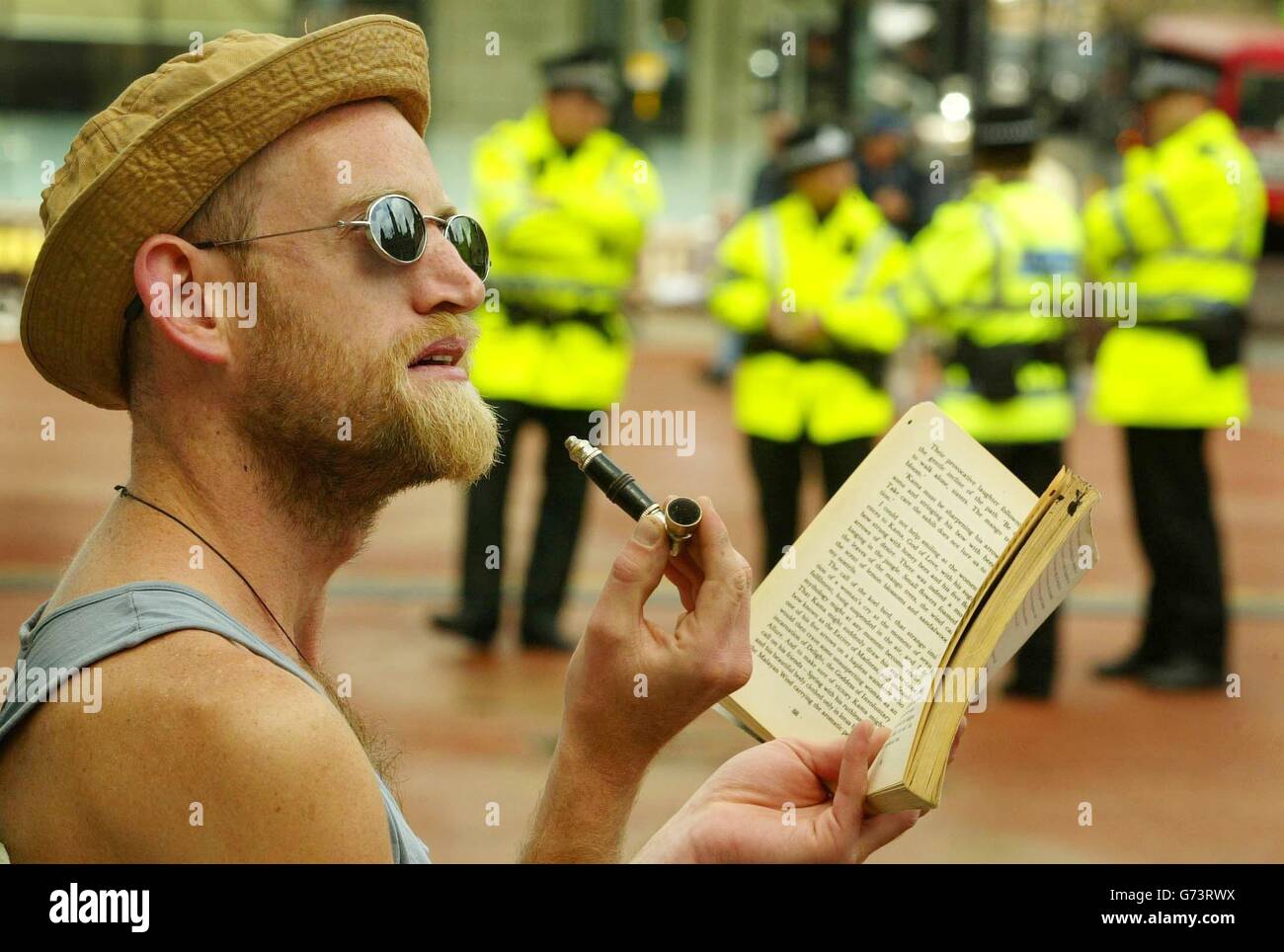 Un dimostratore contro le leggi sulla cannabis che detengono un tubo di cannabis mentre legge un libro prima della marcia da George Square, Glasgow a Kelvingrove Park per lo Smokey Bears picnic, mentre la polizia di Strathclyde guarda sopra. La marcia è stata organizzata dalla Gioventù Socialista Scozzese per aiutare ad aprire le leggi sull'uso della cannabis per tutti. Foto Stock