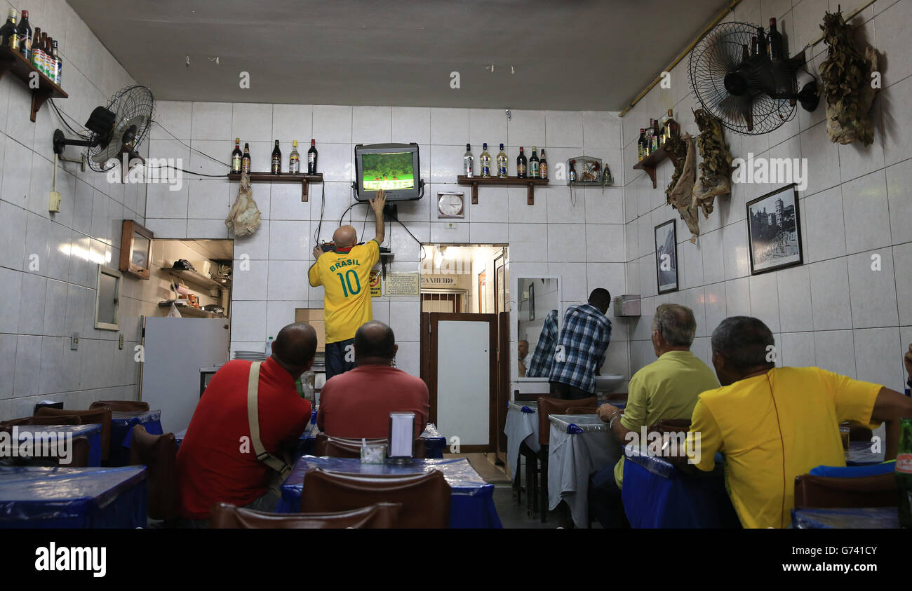 Un proprietario di bar mostra la sua frustrazione nel suo bar centrale Rio de Janeiro, come egli colpisce il televisore per cambiare i colori dello schermo, mentre guarda il gioco con i fan durante il Brasile 0.0 disegnato partita con il Messico Foto Stock