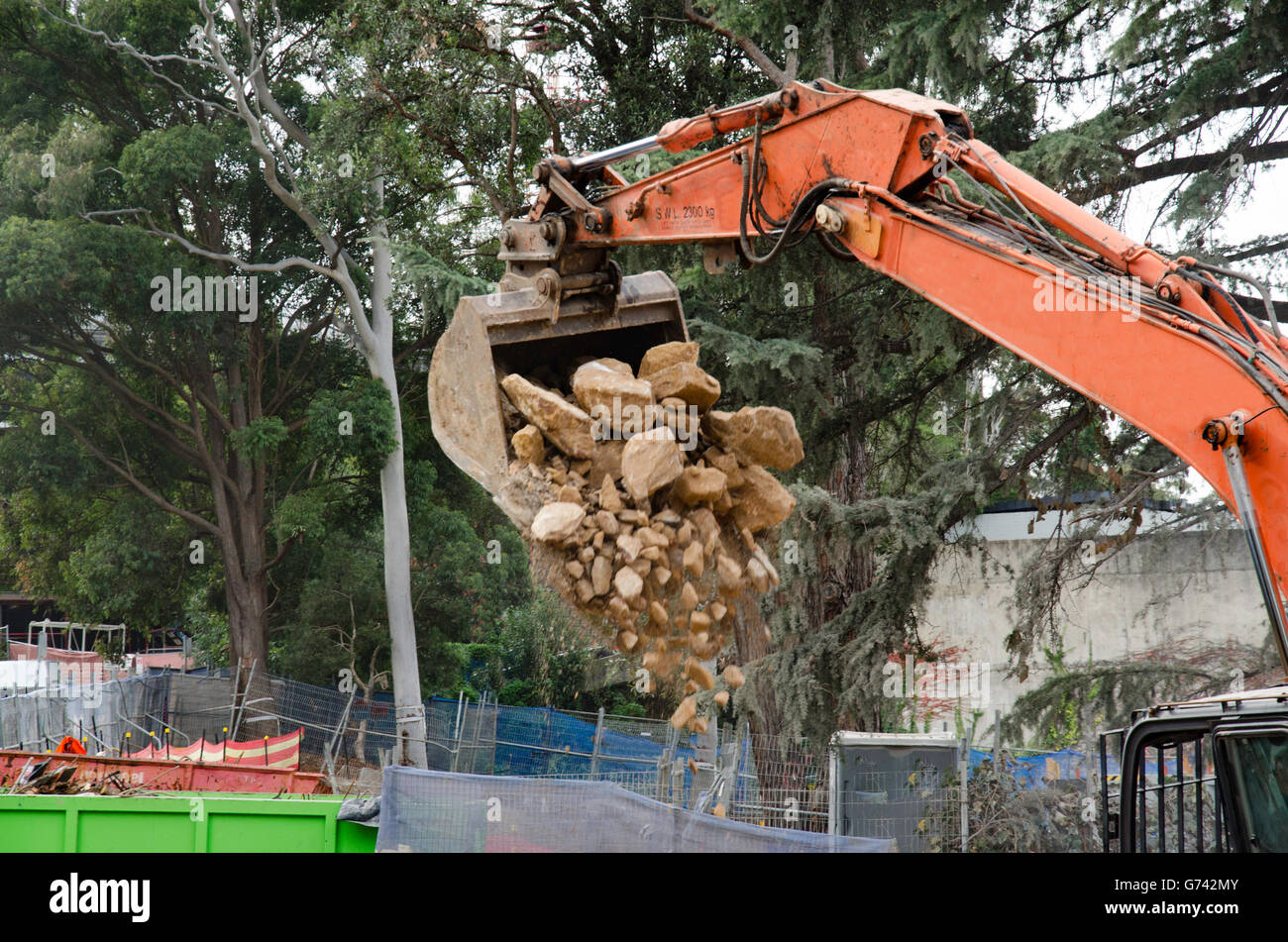 Un ha sollevato il braccio di un escavatore diesel si svuota un carico di rock e macerie sulla costruzione di un sito di lavoro in Australia Foto Stock