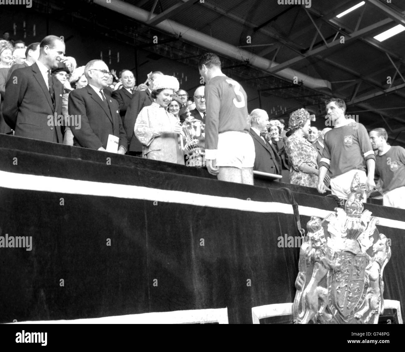 La regina, vestita in lana blu Cambridge con un cappello a petalo abbinato, presenta la fa Cup a Noel Cantwell, a sinistra e capitano di Manchester United, a Wembley. Accompagnata dal duca di Edimburgo, aveva guardato United battere Leicester City 3-1 nella finale di Coppa. Foto Stock
