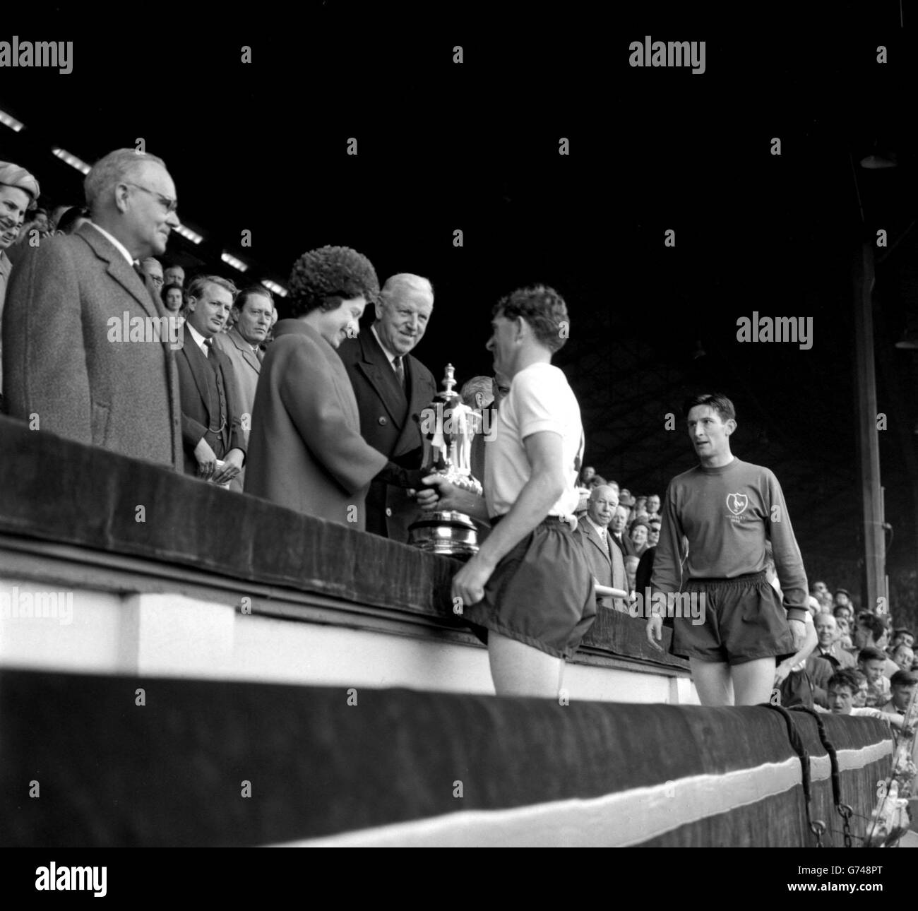Un sorriso e una stretta di mano di congratulazioni da parte della regina per Danny Blanchflower destra-metà e capitano di Tottenham Hotspur, come lei presenta la tazza fa a lui a Wembley. Dietro la coppa c'è Sir Stanley Rous. Sulla destra si trova Bill Brown, il portiere. Spurs ha mantenuto la Coppa per un secondo anno battendo Burnley 3-1 nella finale della Coppa. Foto Stock