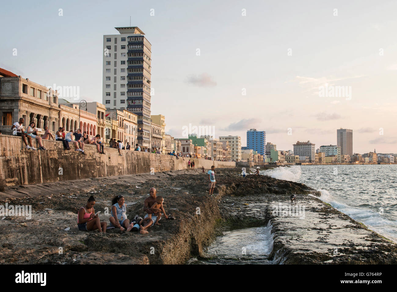 La gente seduta sulla parete del mare di fronte al Malecon (strada costiera) in Havana, Cuba Foto Stock