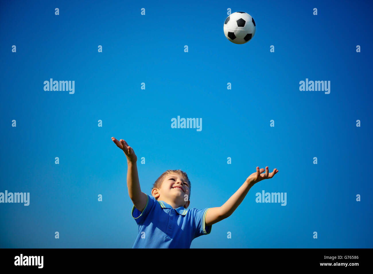 Felice ragazzo giocare a palla, grazioso fanciullo la cattura di palla sul cielo azzurro sfondo, giocando a calcio nella soleggiata giornata estiva Foto Stock